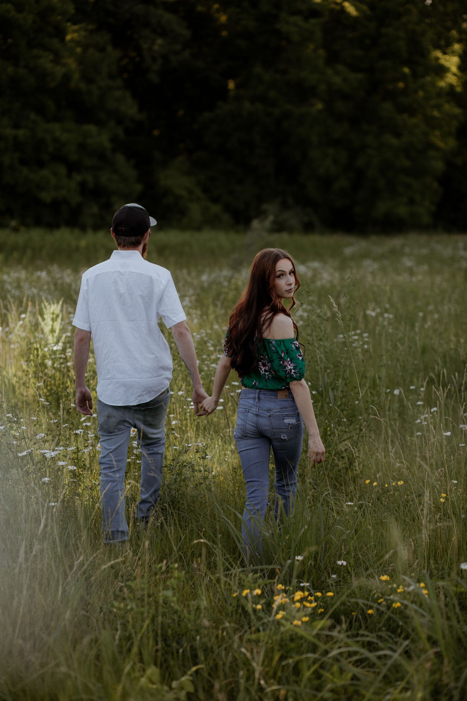 Couple walking hand in hand through a meadow of tall grass and wildflowers.