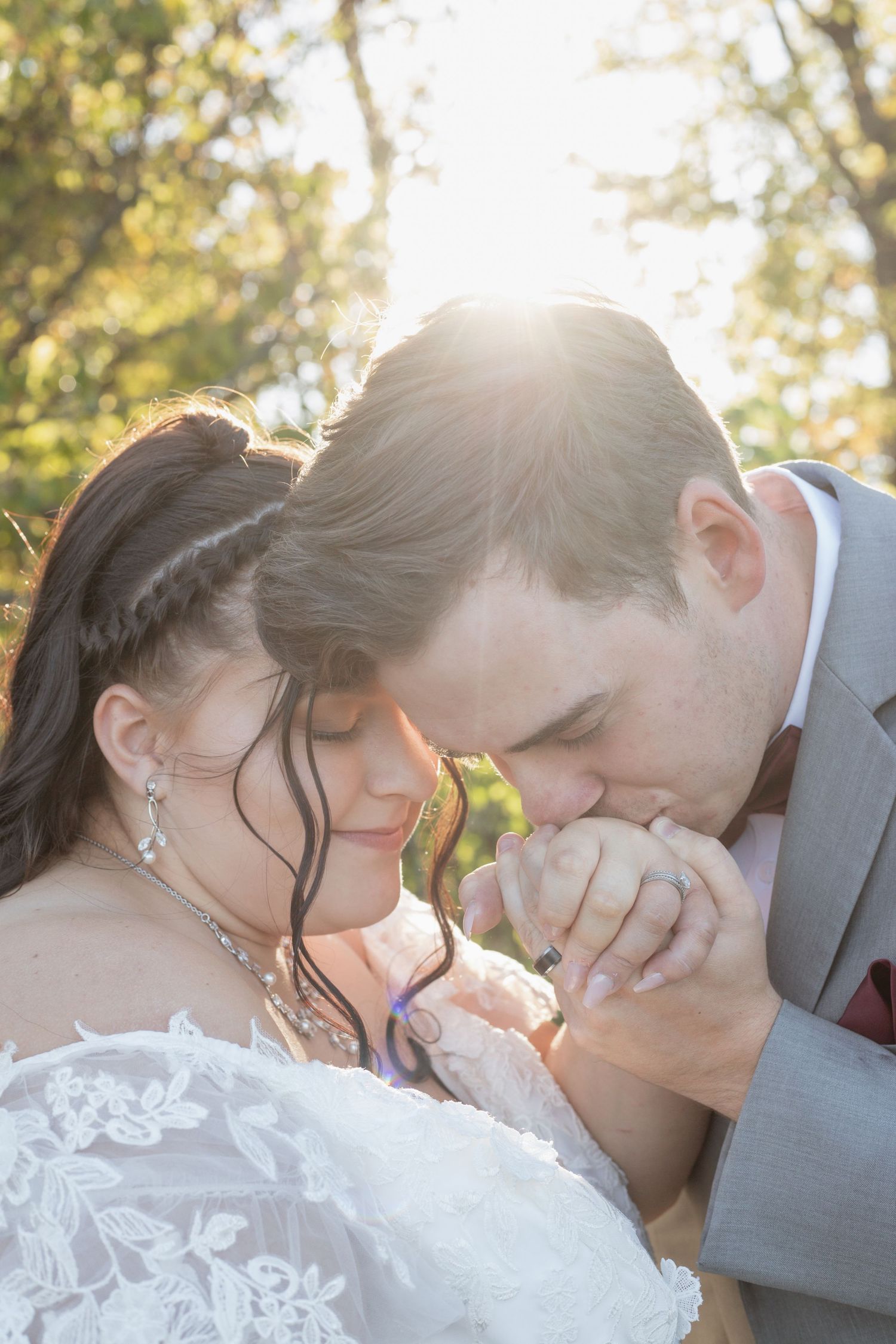 Romantic moment between newlyweds in golden sunlight as groom kisses bride's hand during outdoor wedding ceremony.