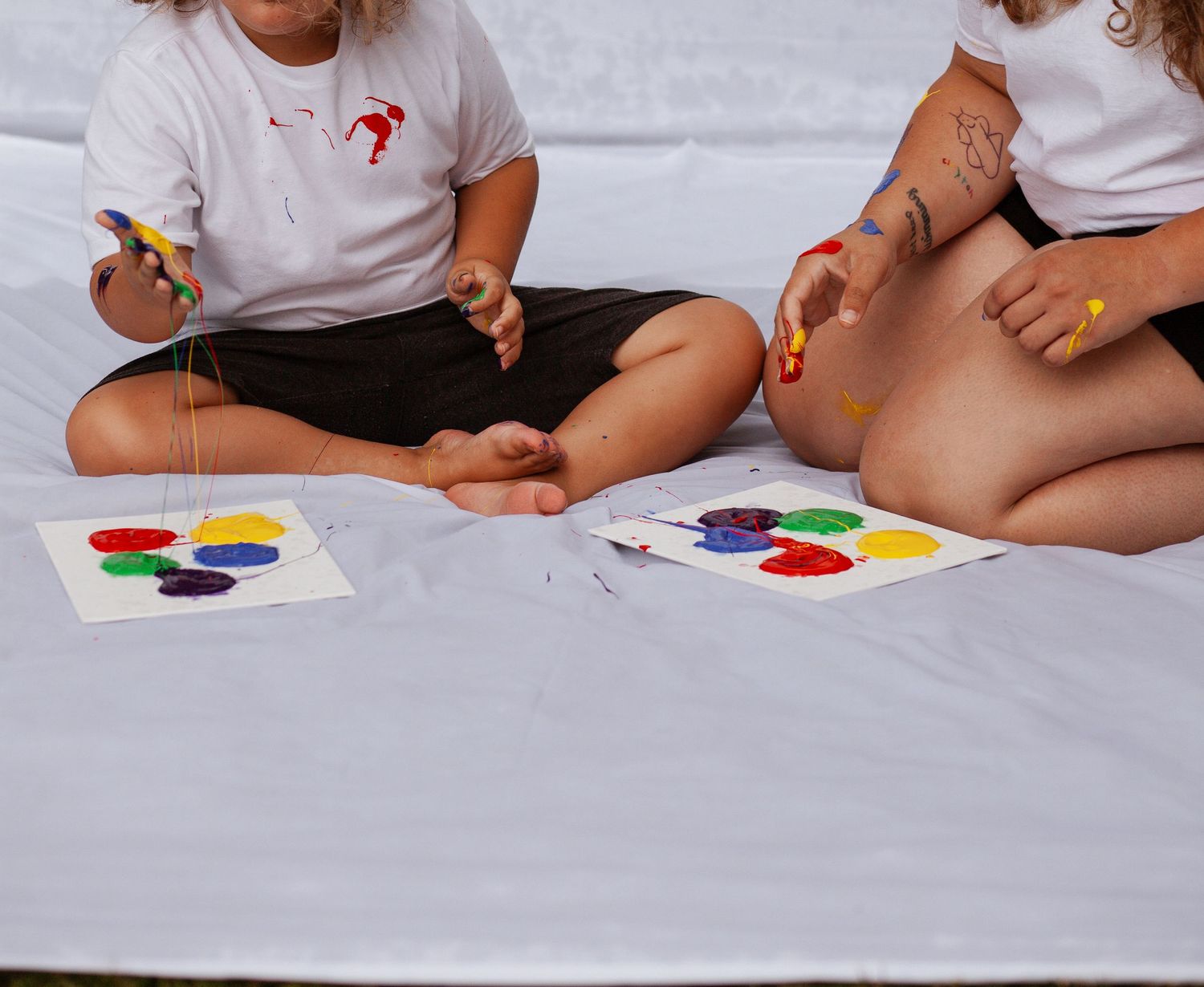 Children sitting on white surface playing with colorful art supplies.
