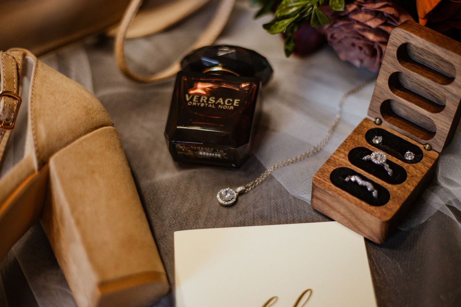 Wedding rings and accessories styled on wooden surface with warm lighting.