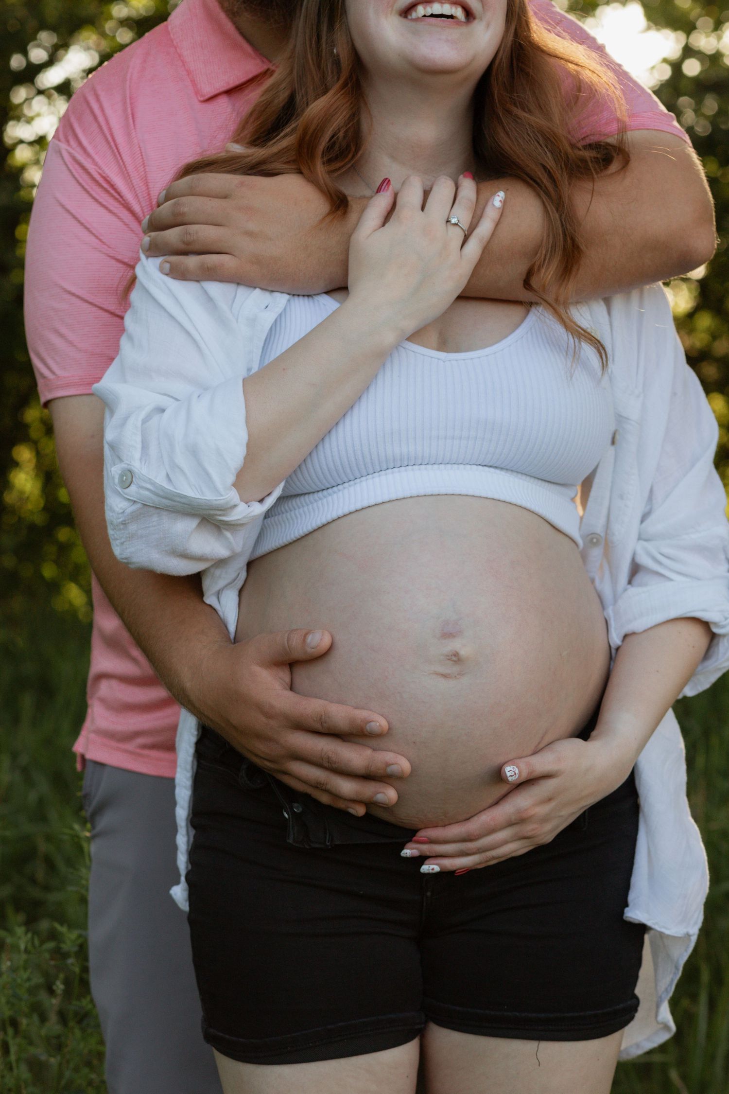Outdoor maternity photoshoot featuring a pregnant belly in white crop top and flowing white shirt.