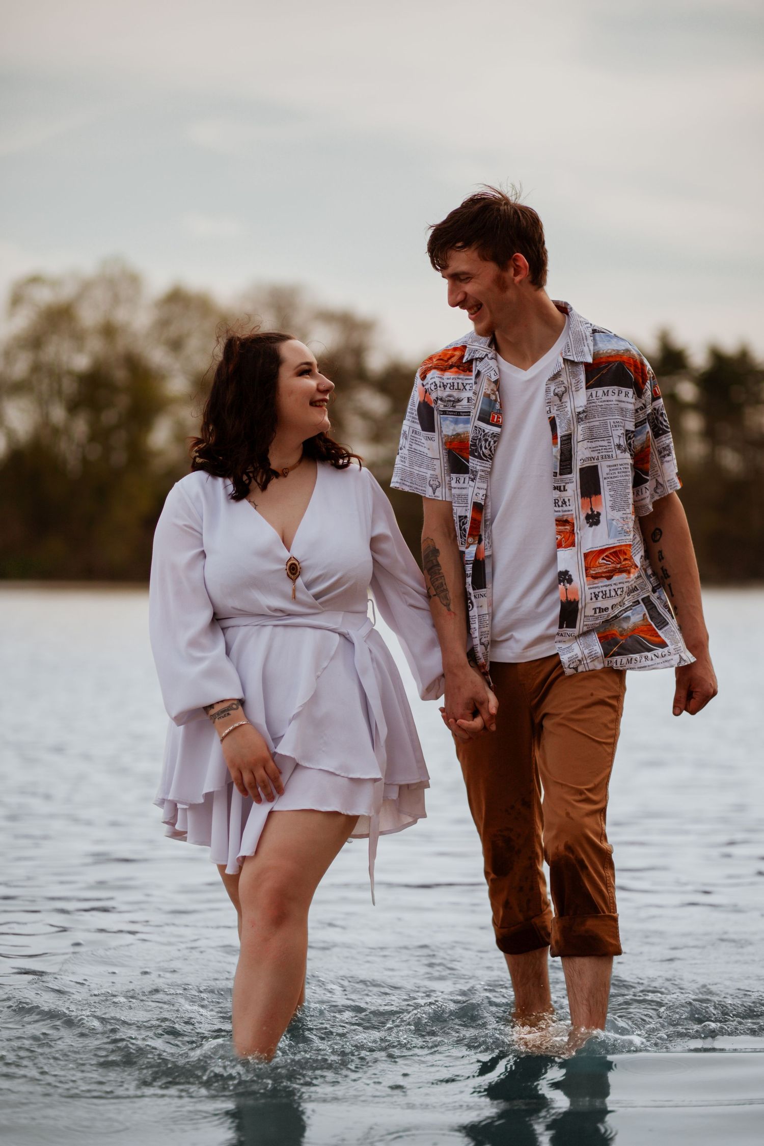 Joyful couple walking through shallow water wearing casual summer outfits.