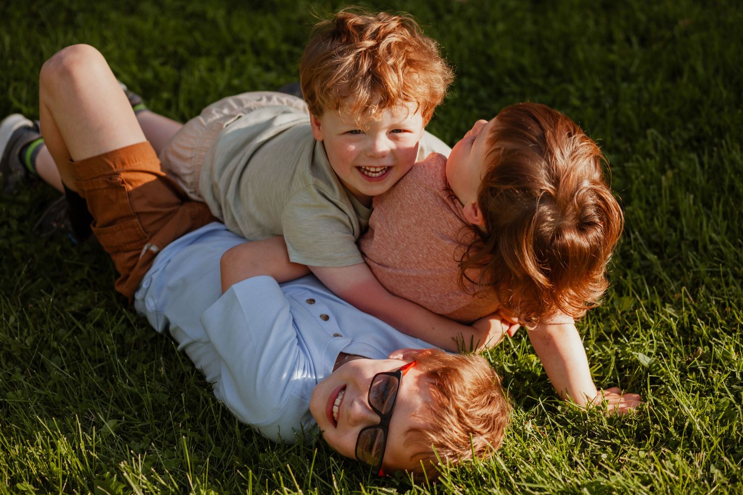 Family lying together on green grass in warm sunlight.