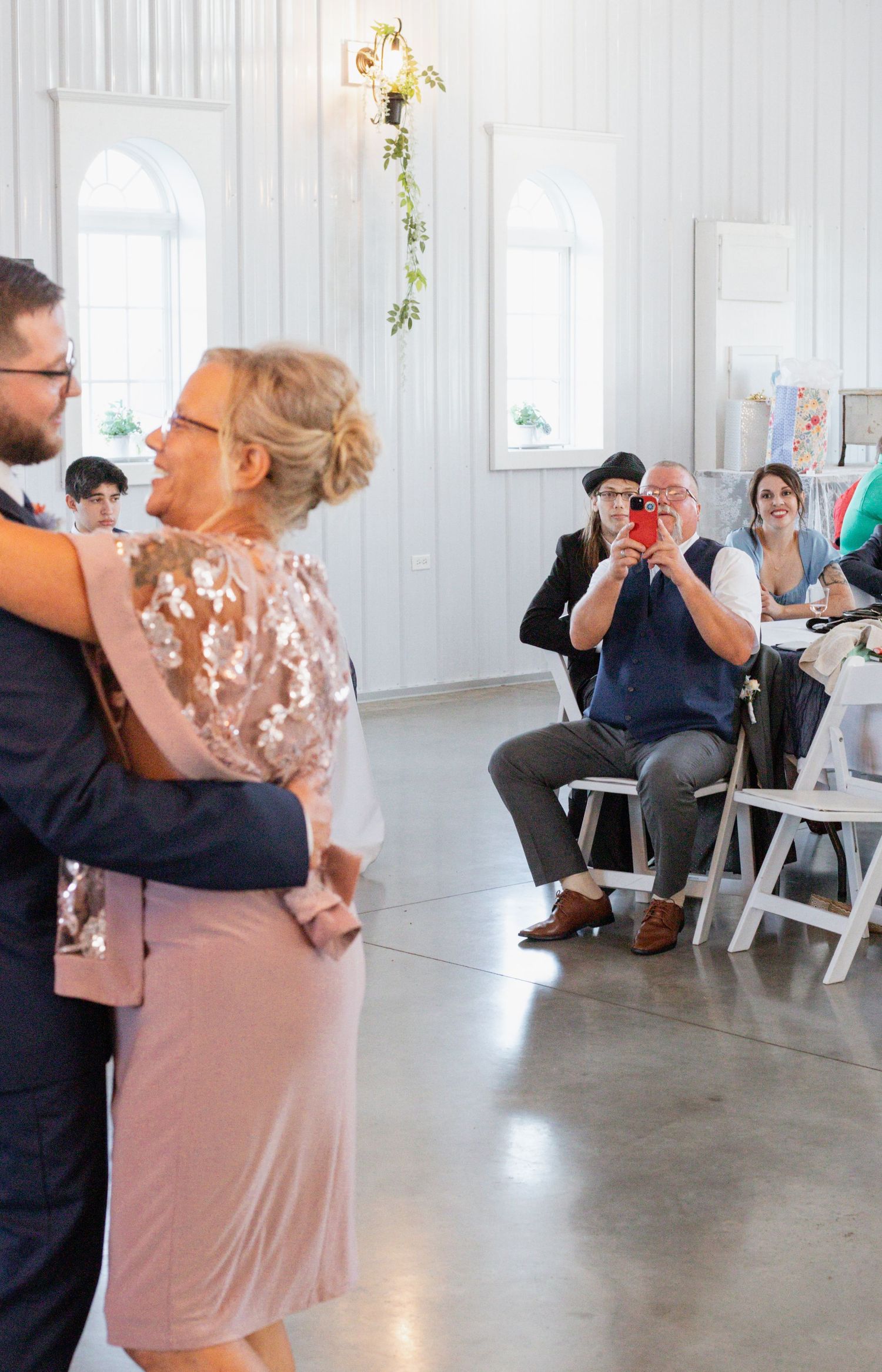 Wedding guests dancing in an elegant white chapel-style venue with arched windows.