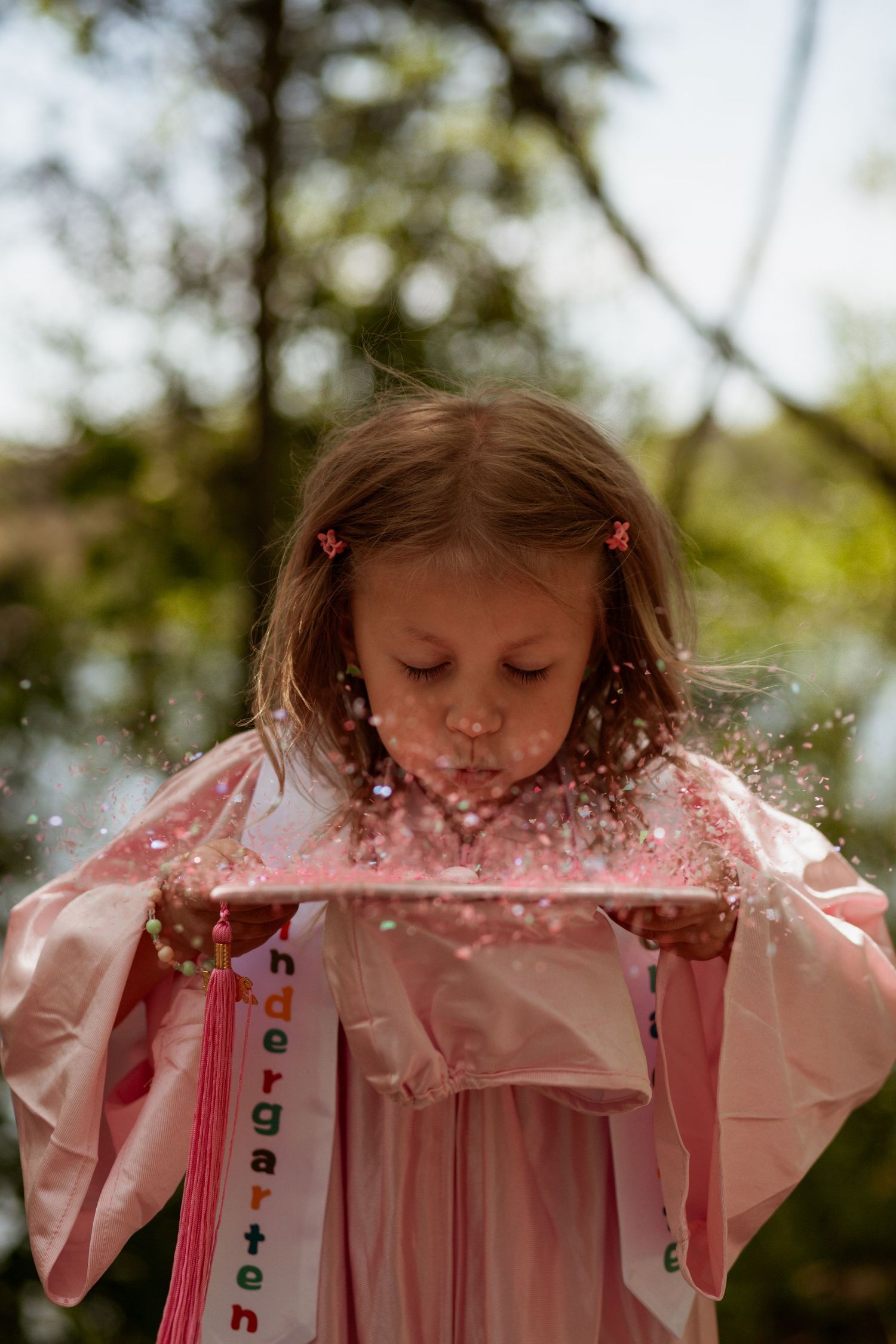 Young child in pink raincoat blowing glitter or sparkles in outdoor setting.