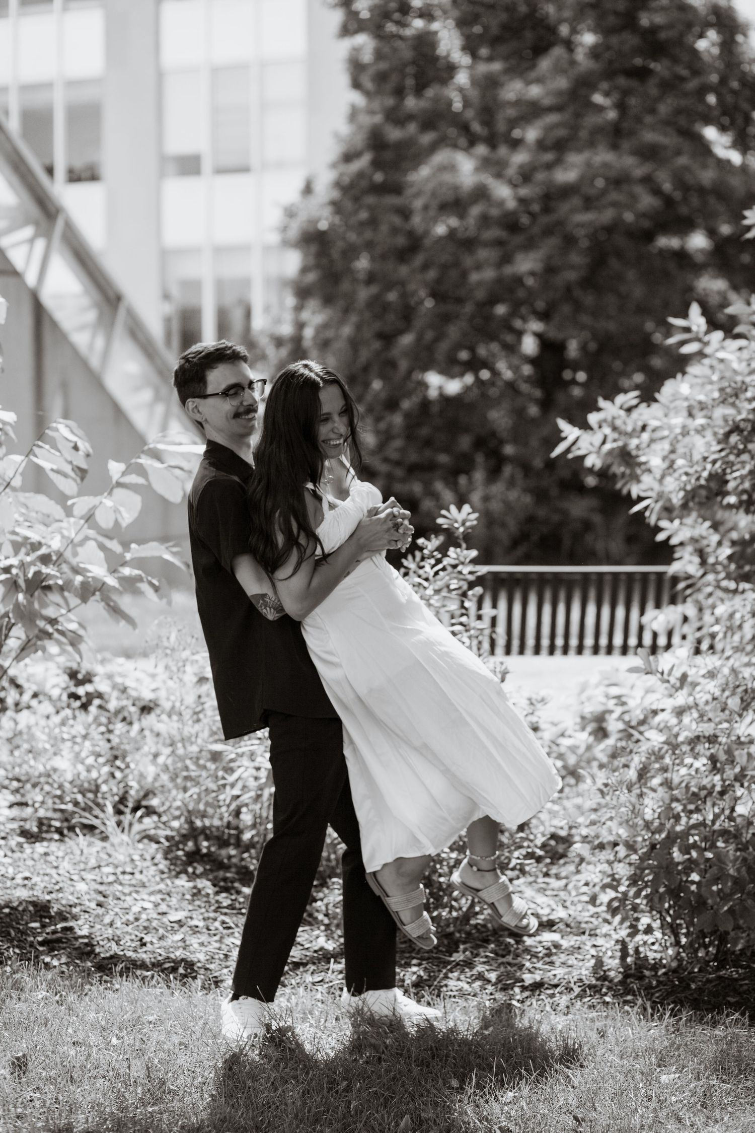 A romantic black and white wedding photo series showing a couple dipping and kissing in a garden setting.