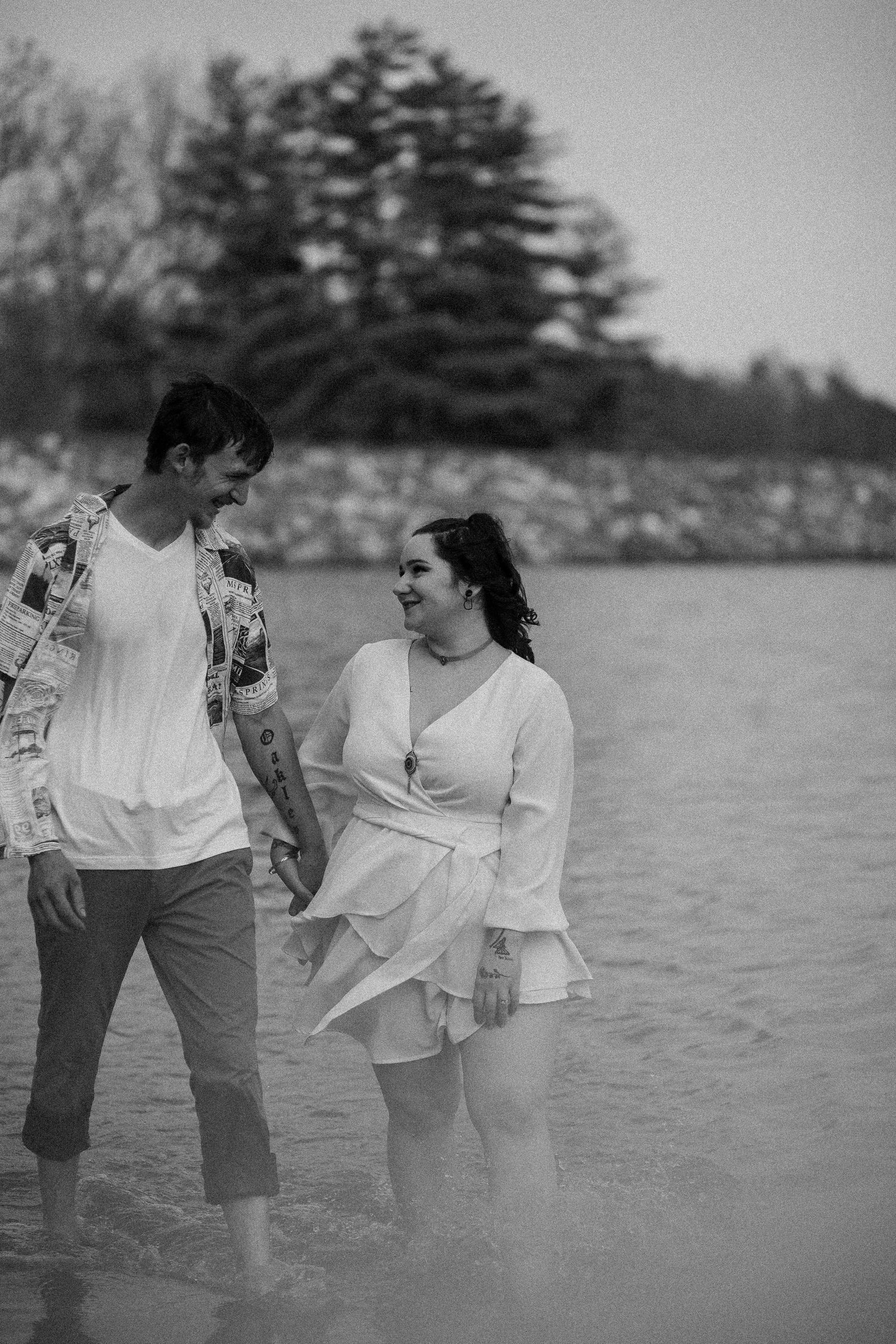 Black and white photo of couple walking along shoreline sharing a laugh.