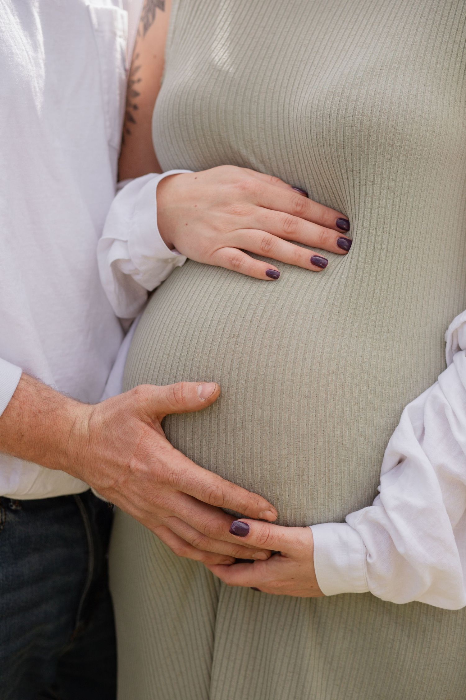 Hands gently resting on a pregnant belly wearing a ribbed beige sweater.