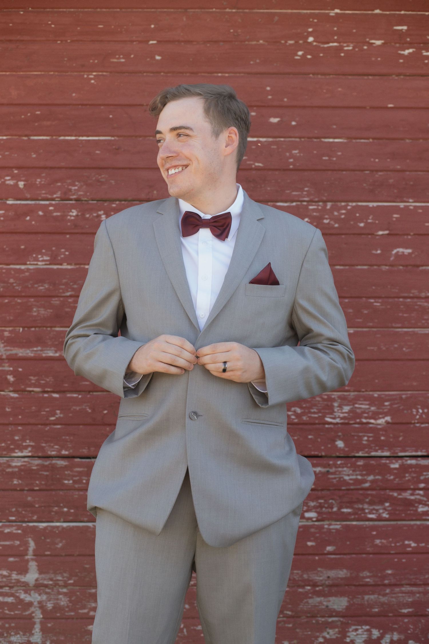 Gray suit and burgundy bowtie against weathered red barn siding.