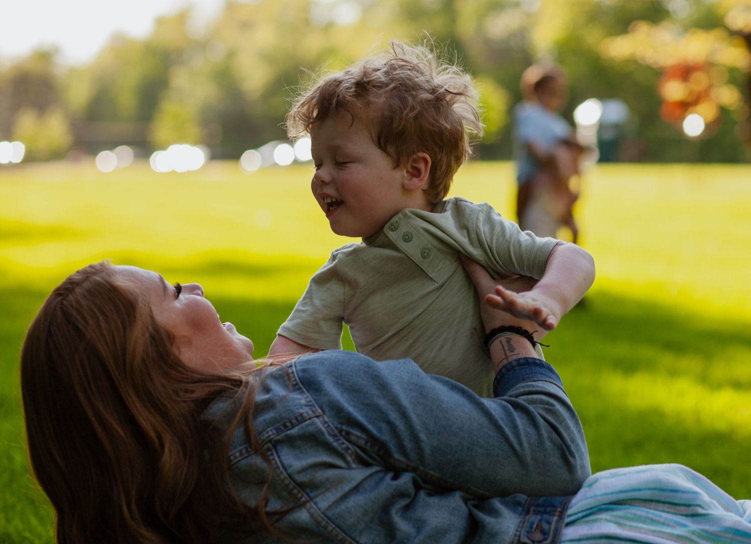 A candid moment of family bonding while lying on grass in a sunny park.