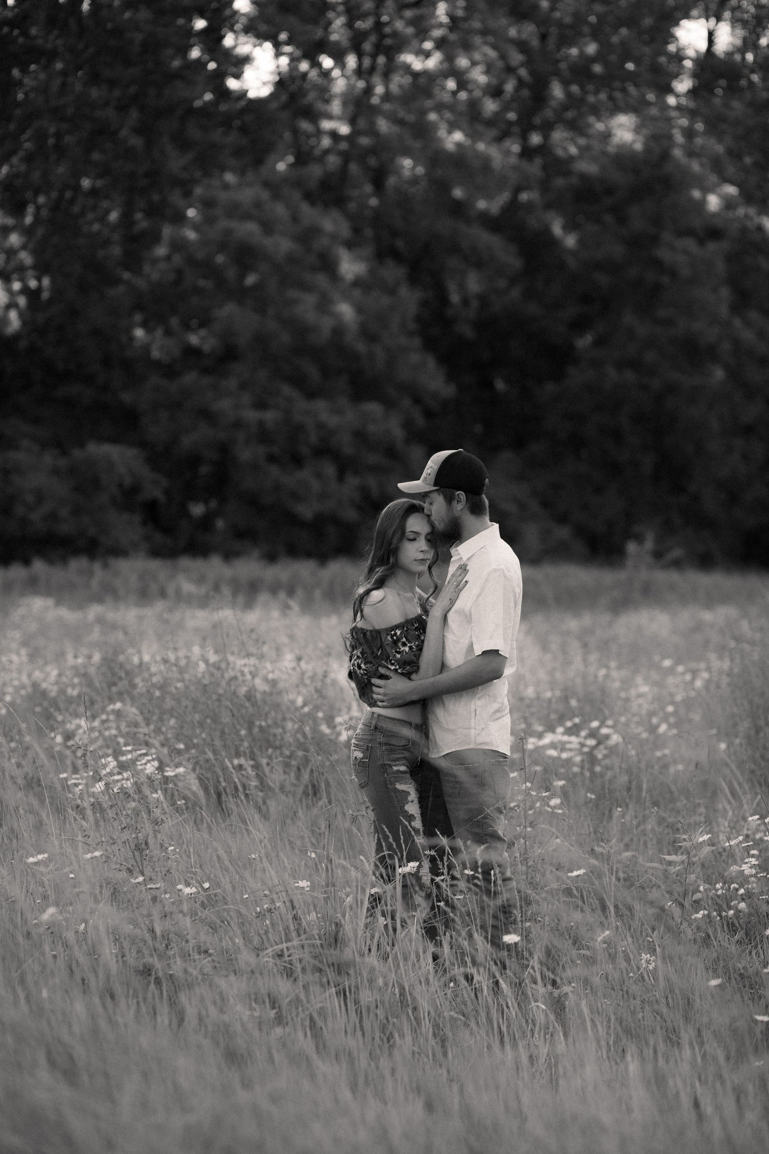 Black and white photo of a couple embracing in a wildflower field at dusk.