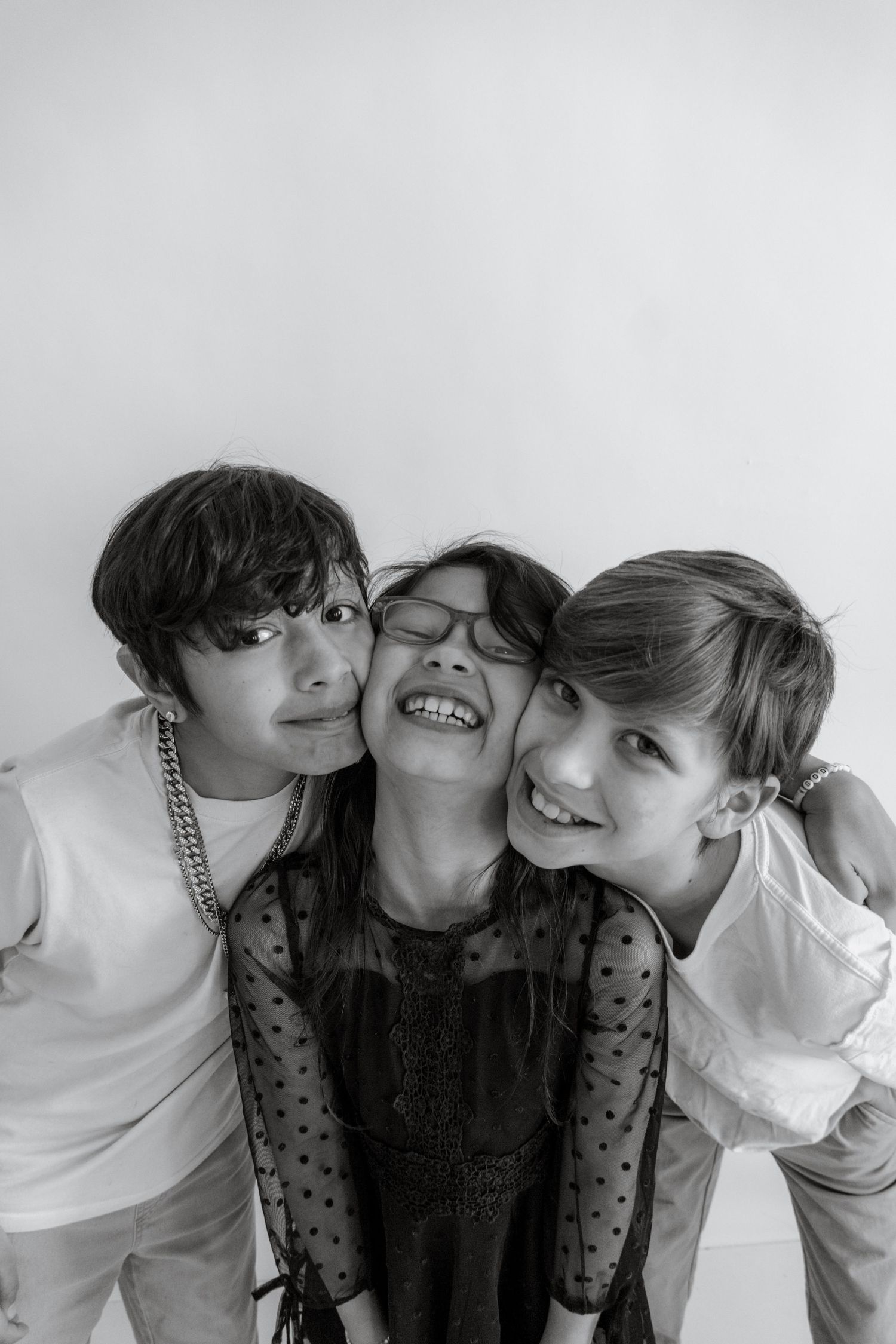 Black and white portrait of three siblings sharing affectionate moments.