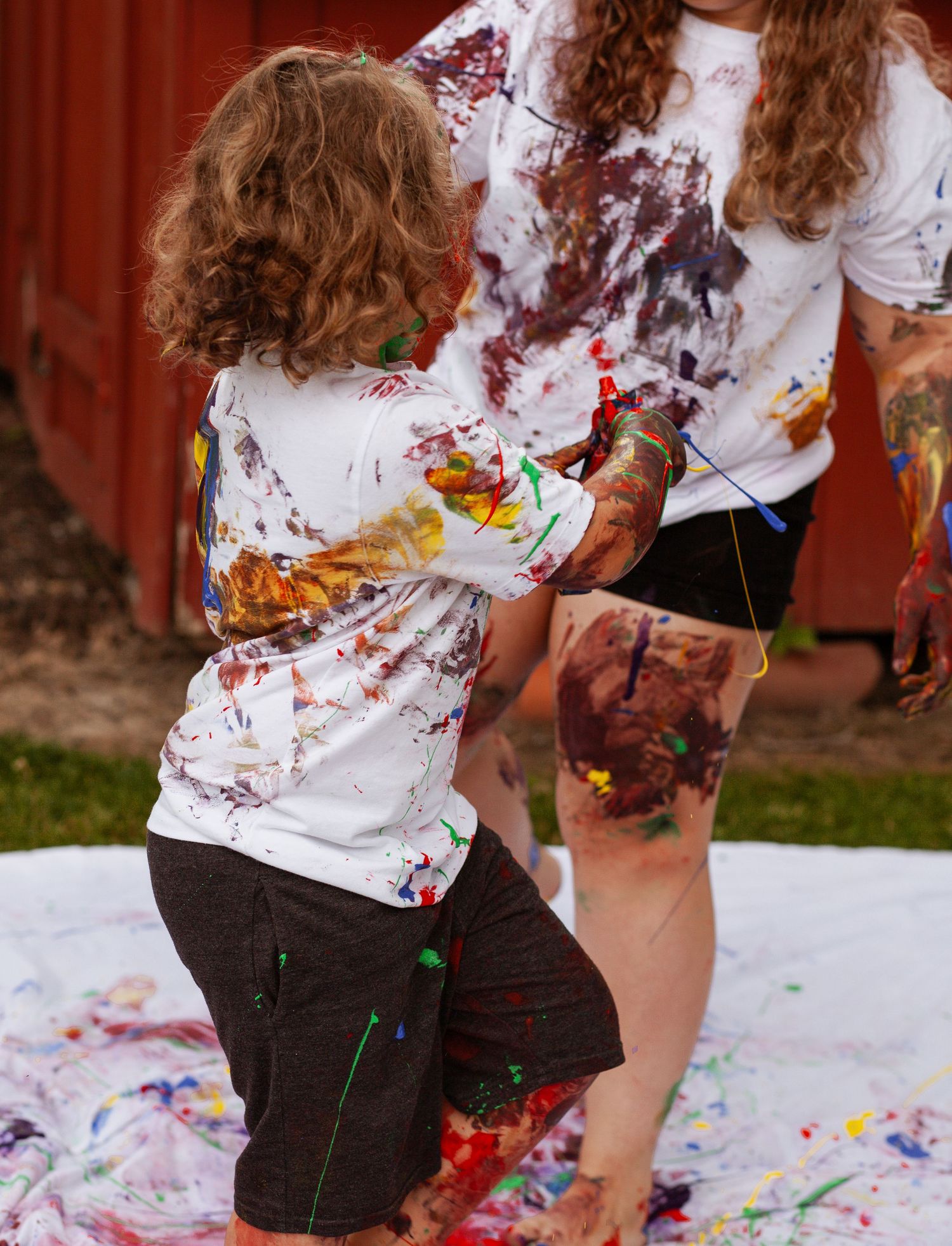 Paint-splattered figures create colorful artwork on white surface outdoors.