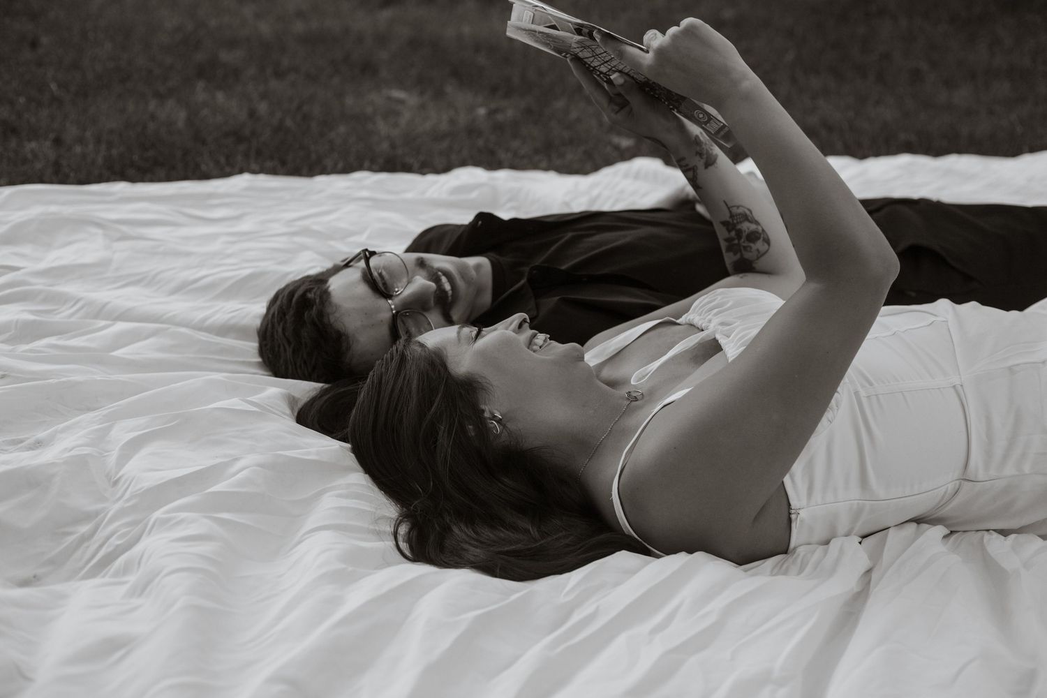 Person lying down on white sheets in dramatic black and white photography.