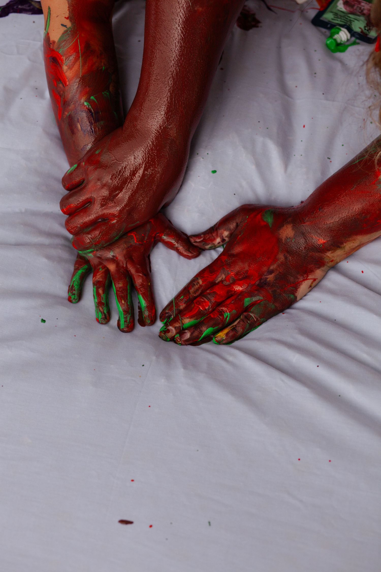 Hands and feet covered in red and green paint make marks on white fabric.