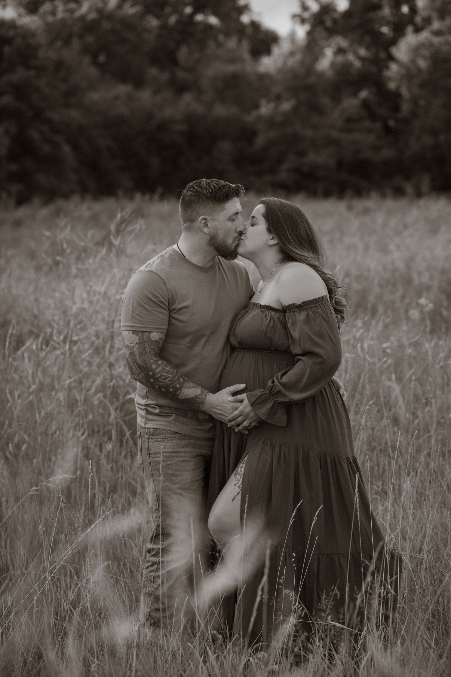 Black and white photo of a couple sharing an intimate moment in a grassy field.