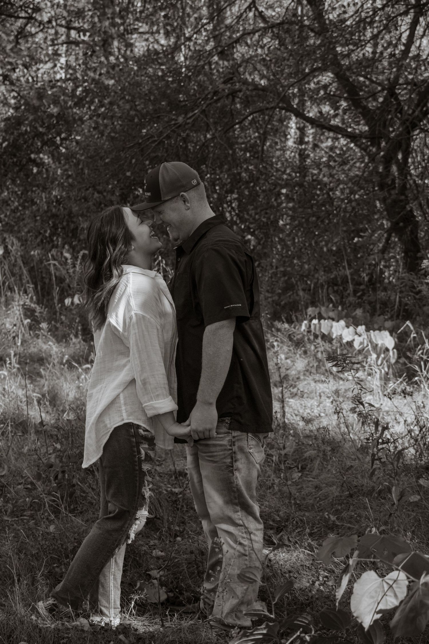A couple sharing a sweet kiss in a wooded area captured in black and white.