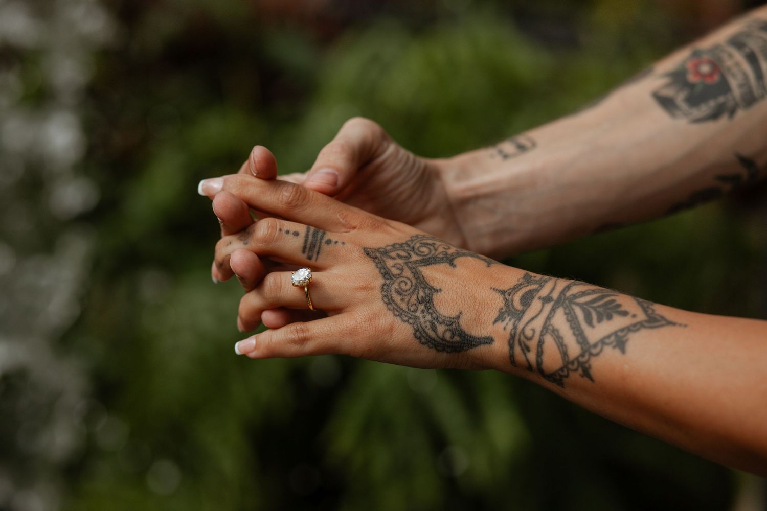 Close-up of tattooed arms and hands against a natural background.