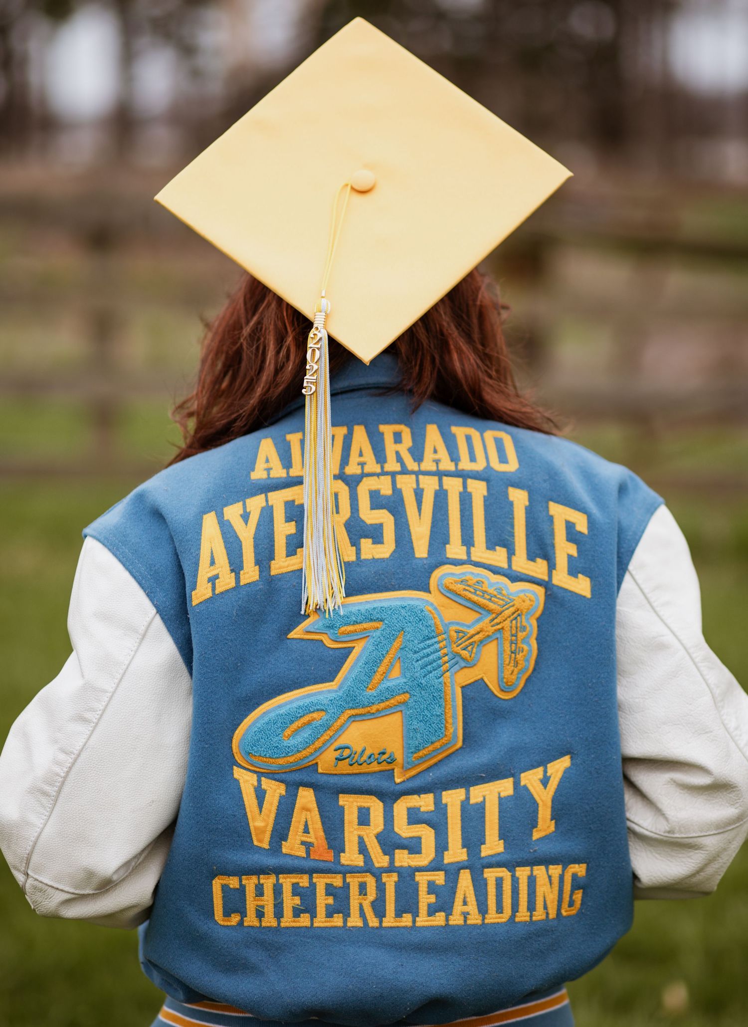 Blue varsity cheerleading jacket with gold lettering displayed outdoors.