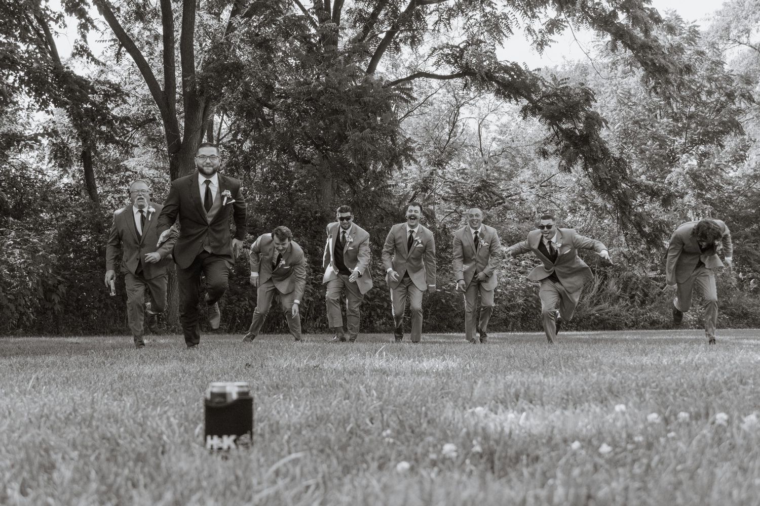 A black and white photo of groomsmen sitting in a row on a grassy hill.