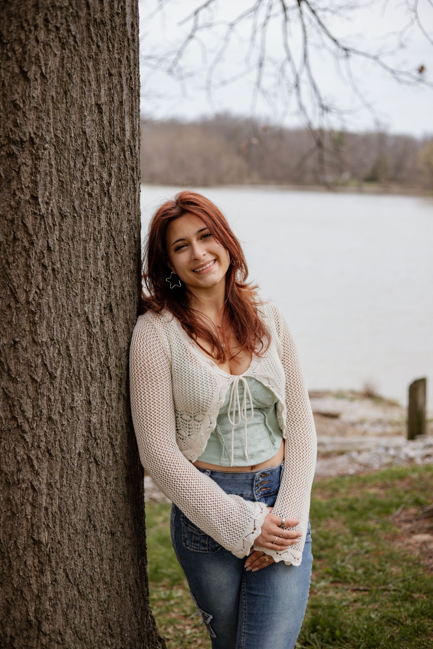 Outdoor portrait session near tree trunk showing casual style with knit sweater and denim.