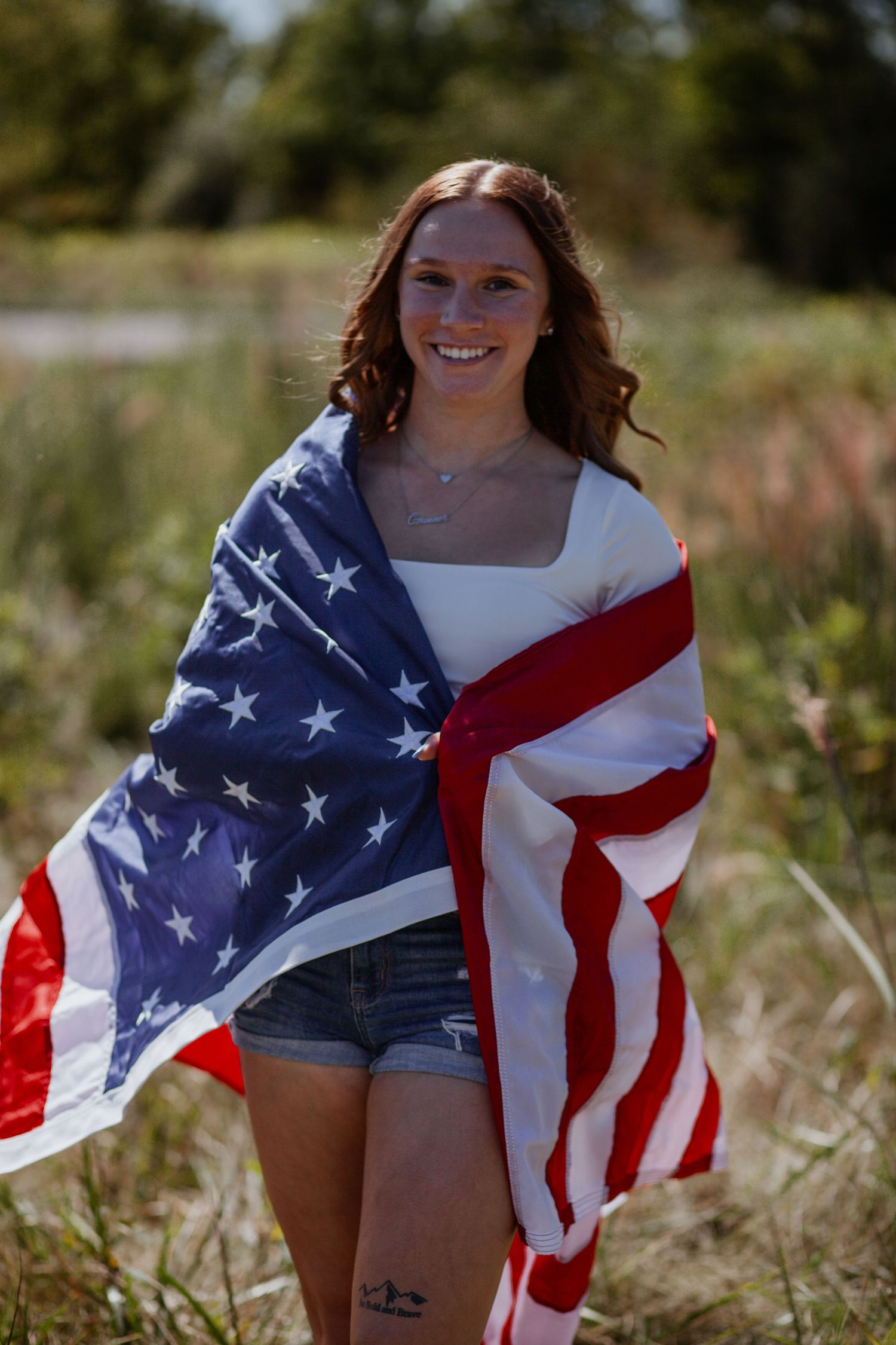 American flag waving in a sunny meadow with tall grass.