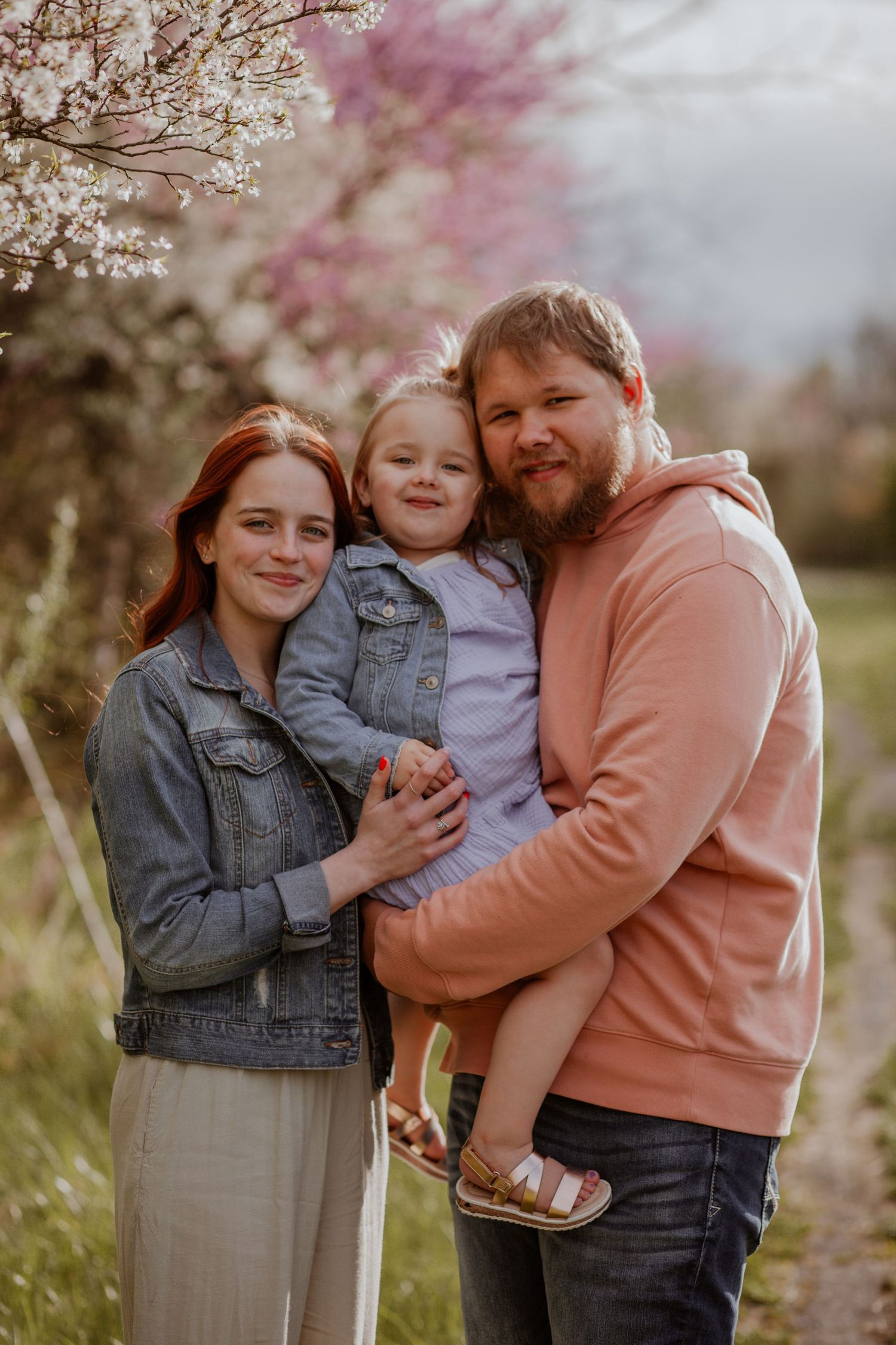 Family embracing under blooming cherry blossoms in spring setting.