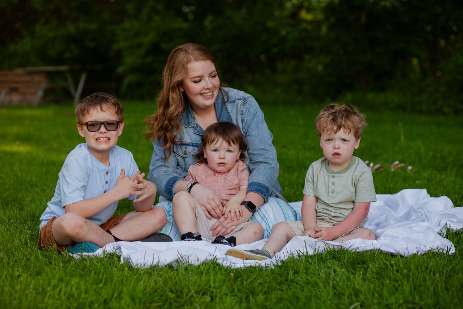Family group relaxing together on blanket in sunny park setting.