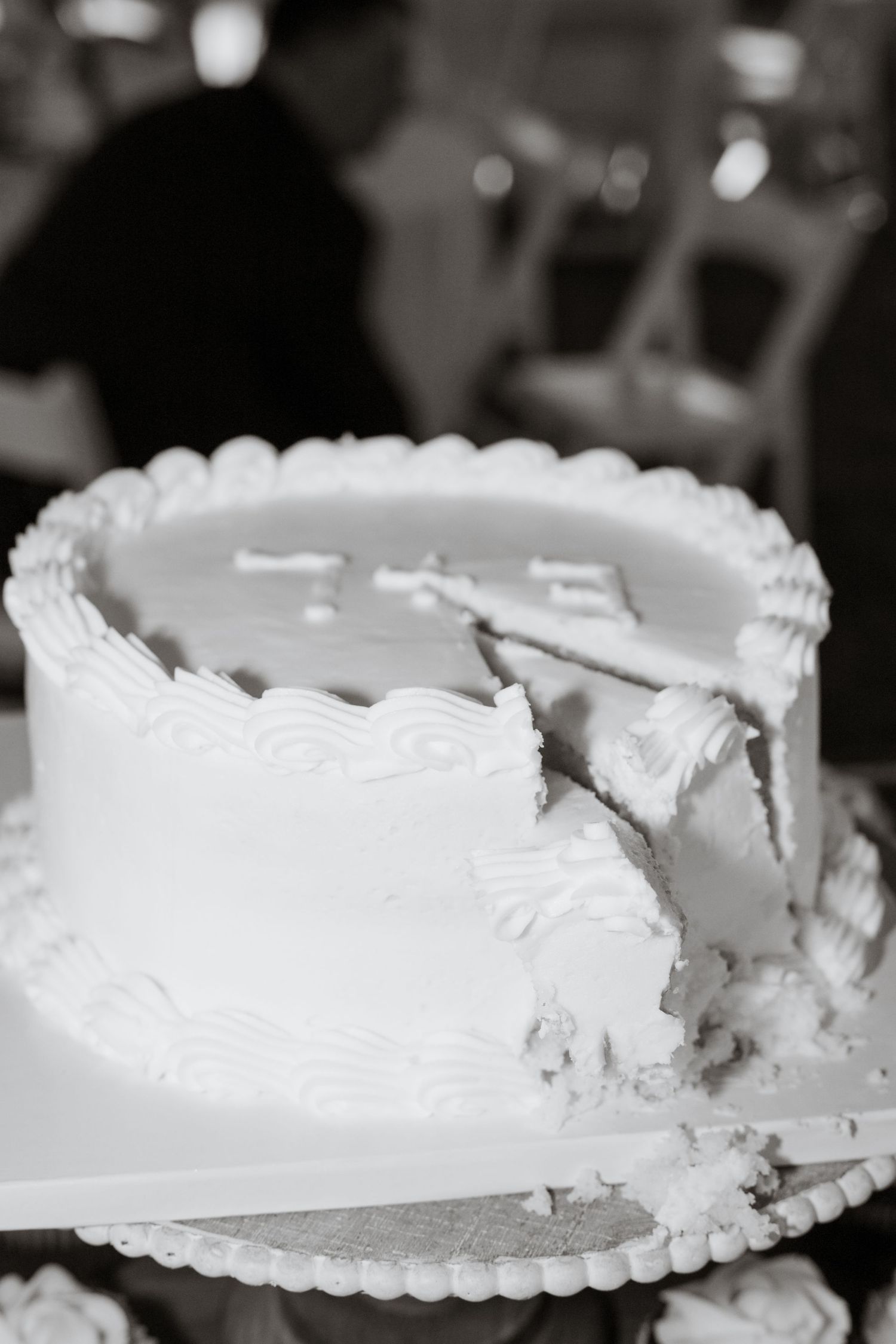 White wedding cake with traditional frosting showing a slice being cut out.