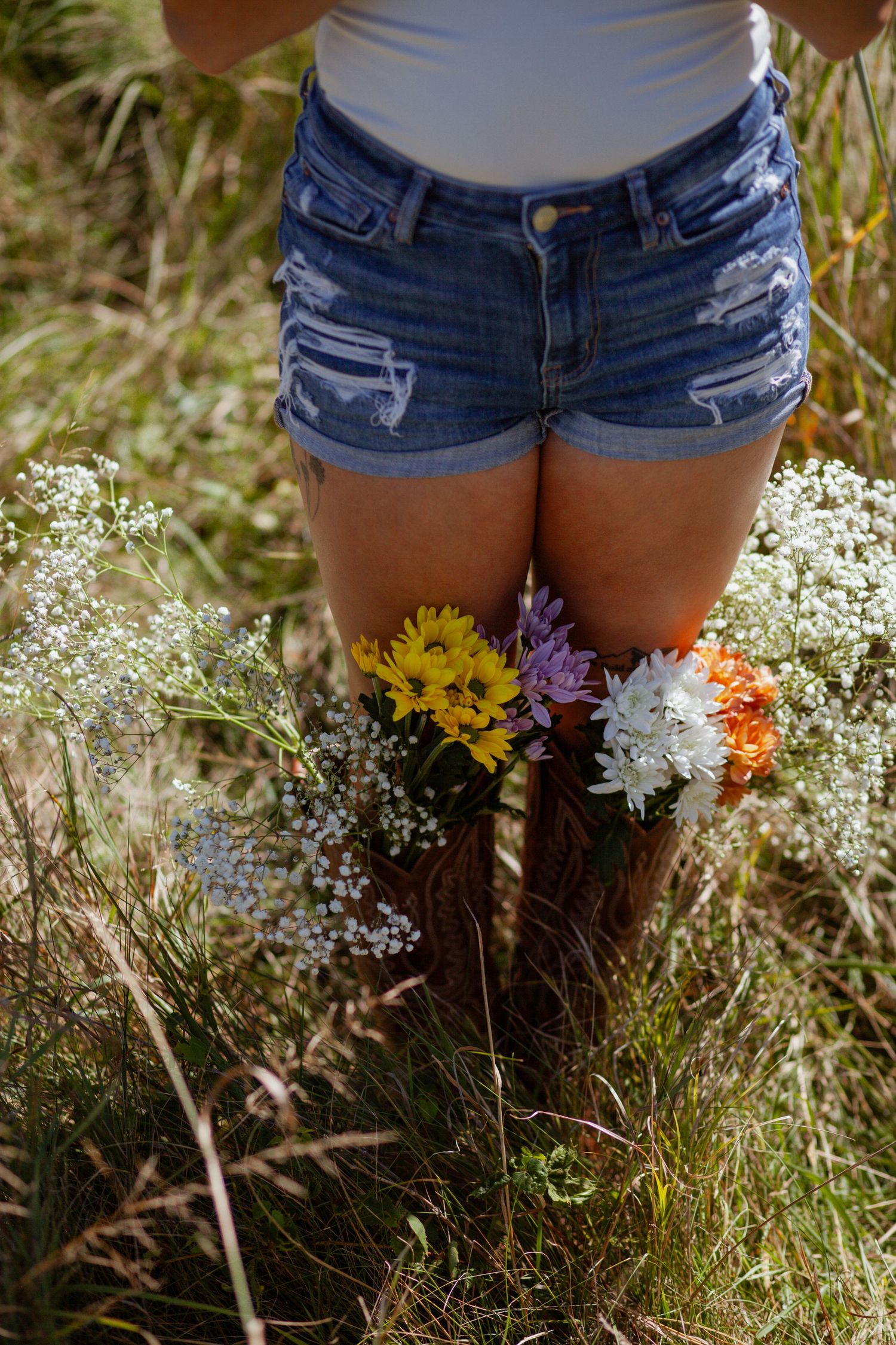 Close-up view of denim shorts with wildflowers and white baby's breath flowers in a sunny meadow.