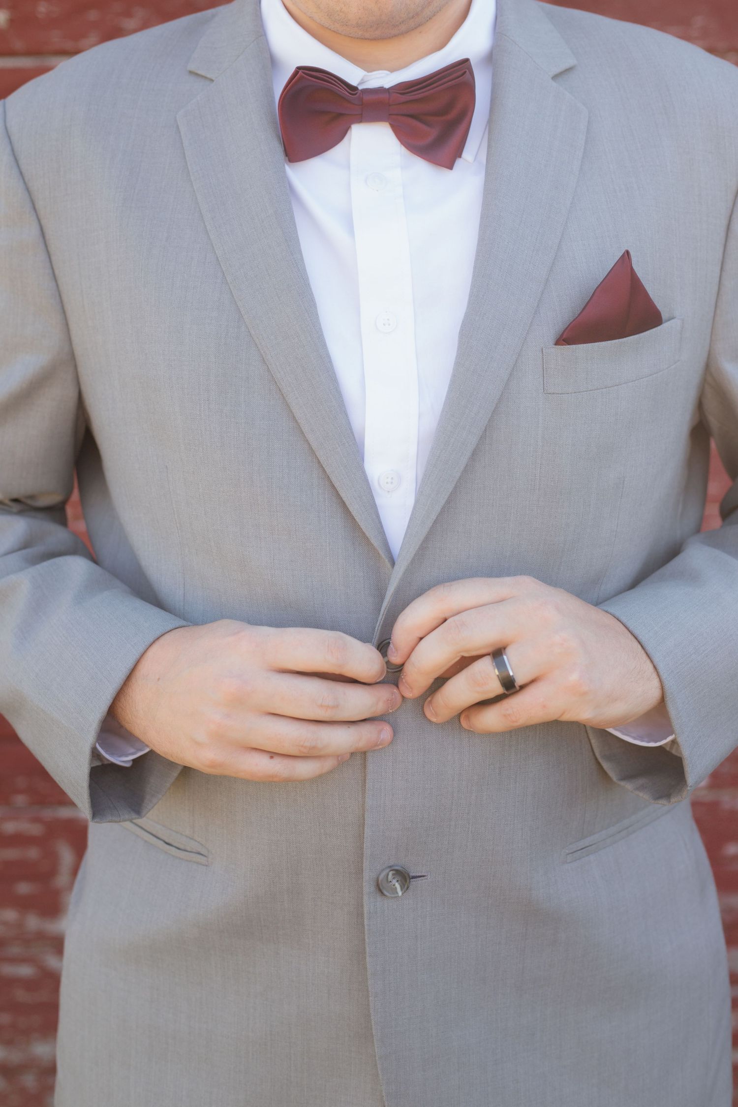 Close-up of a gray suit jacket with burgundy bowtie showing details of formal wedding attire.