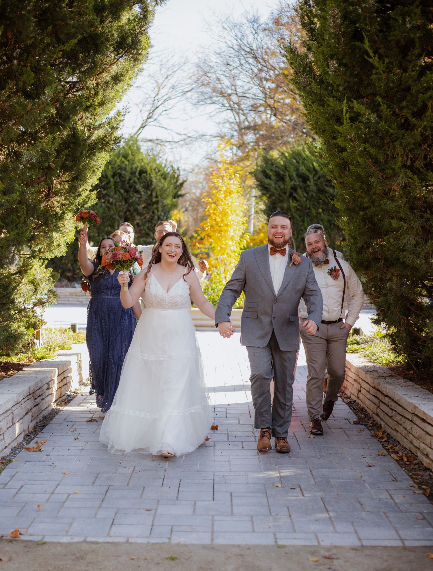 Wedding party walks and laughs together on stone pathway.