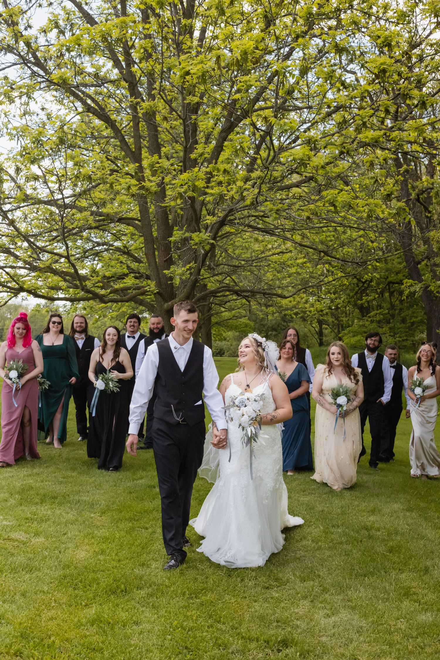 Wedding party poses for fun group photos under blooming spring trees in a grassy outdoor setting.