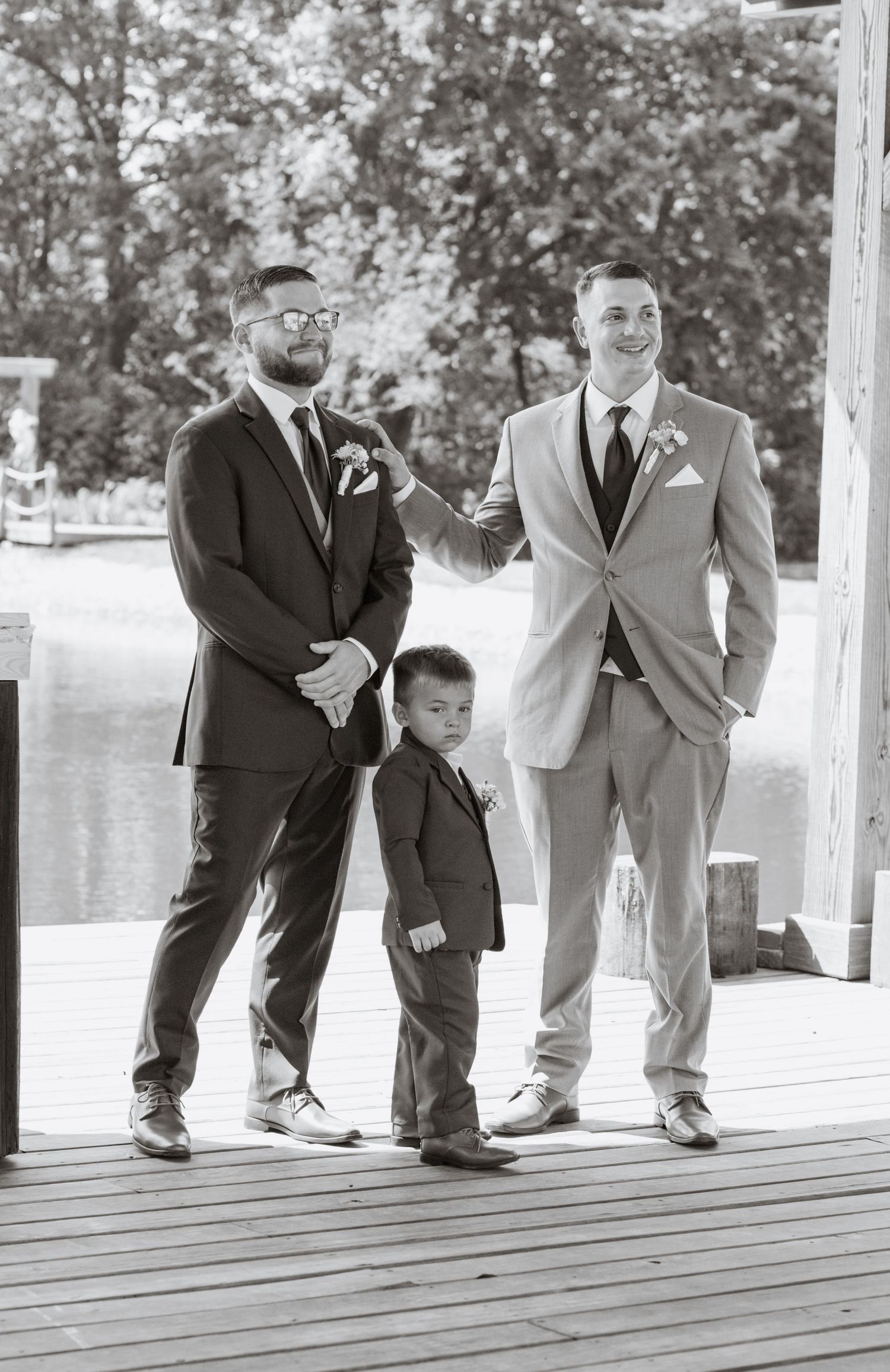 Black and white photo of groomsmen and young ring bearer standing on wooden deck.