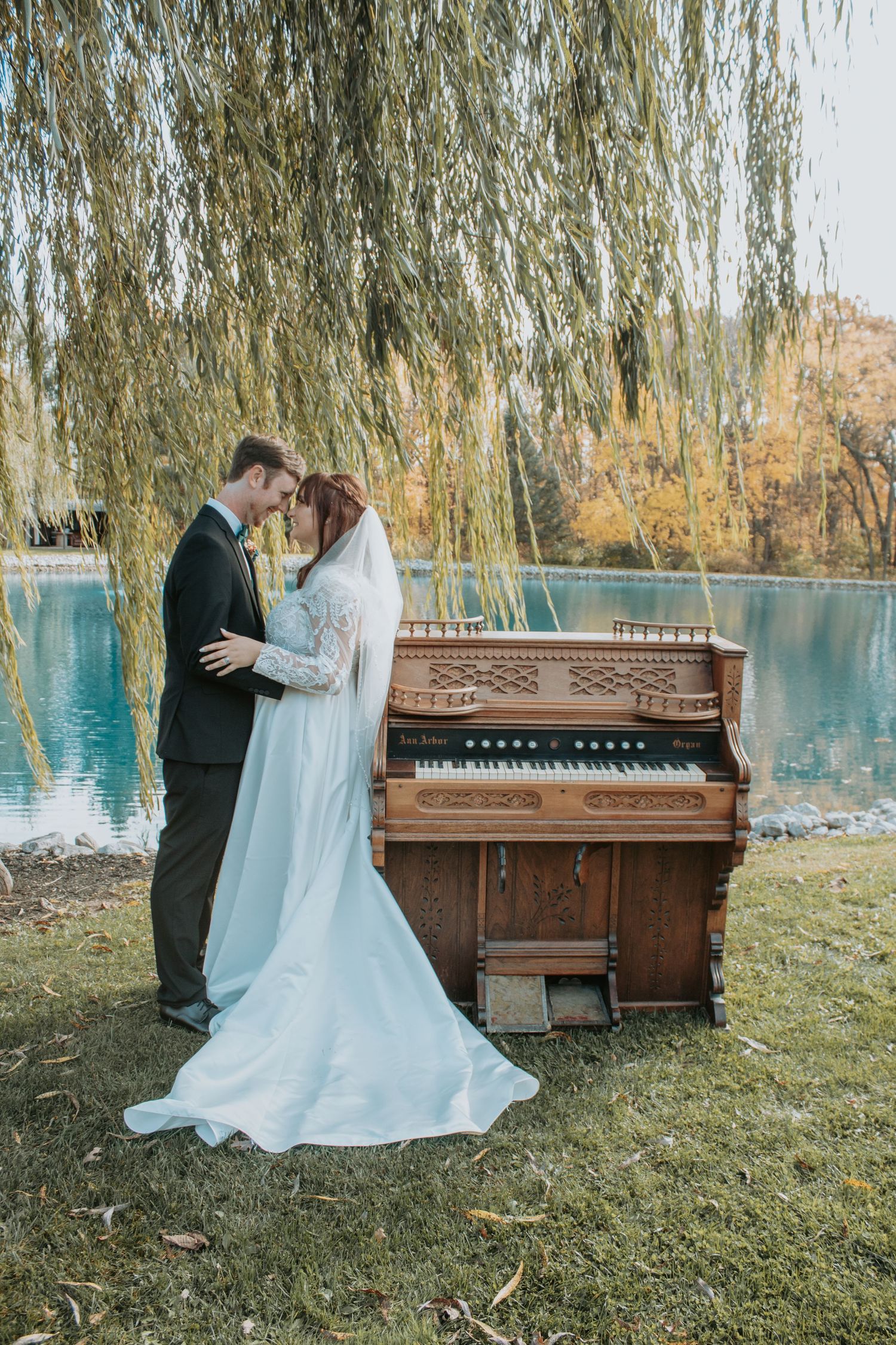 Wedding couple posing by vintage piano under weeping willow tree.