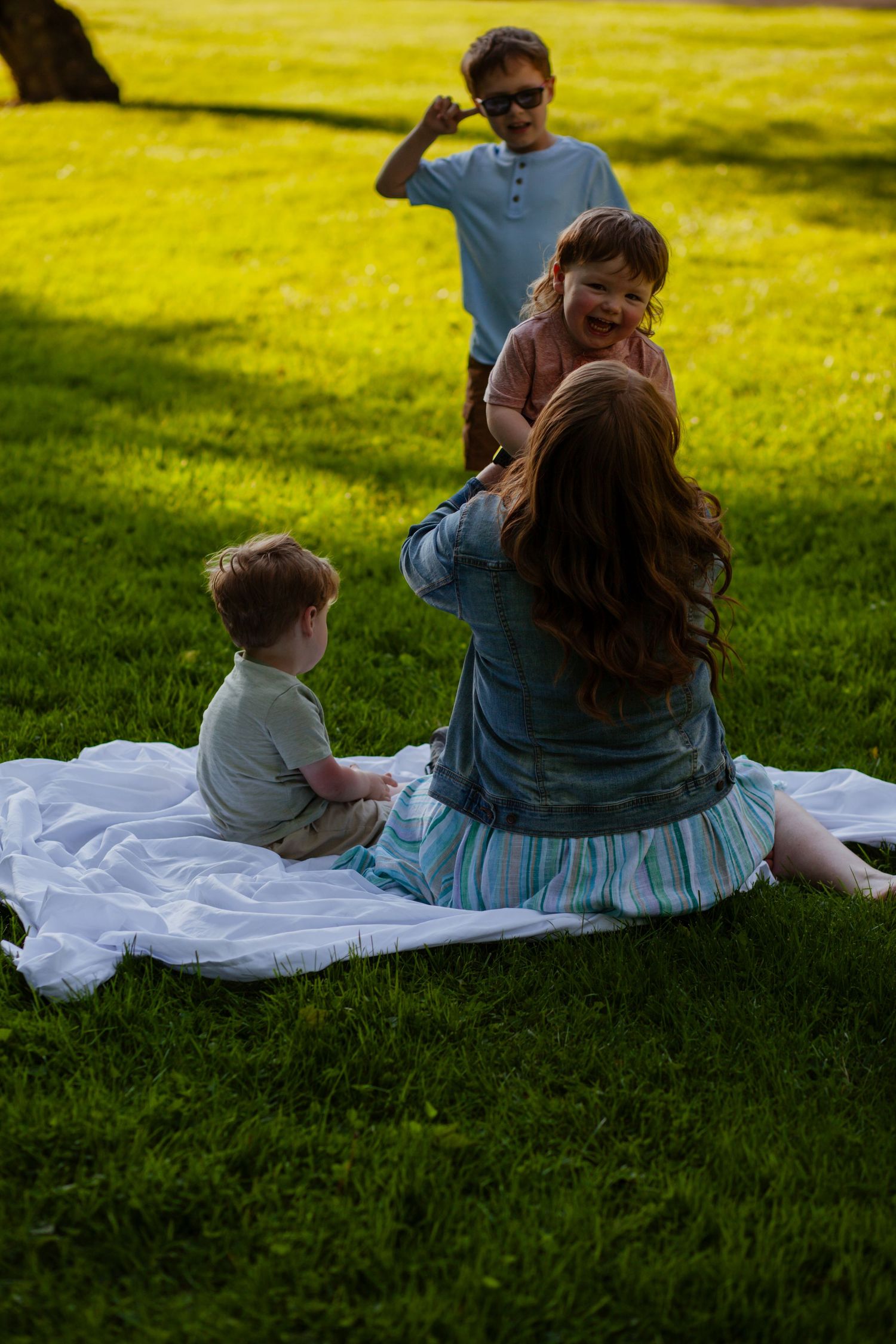 Family relaxing together on a white blanket in a sunny green field.