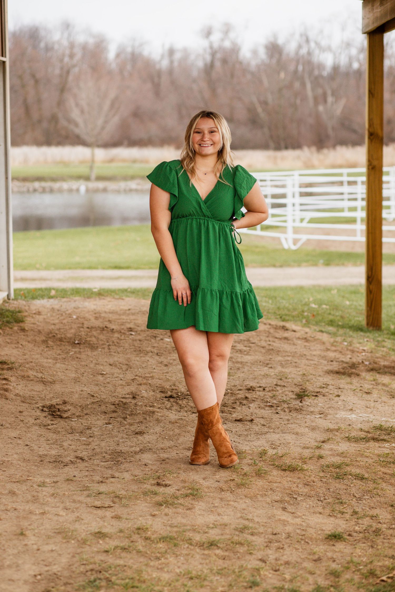 A photo series featuring a green dress and brown boots in a rustic barn setting with white fences in background.