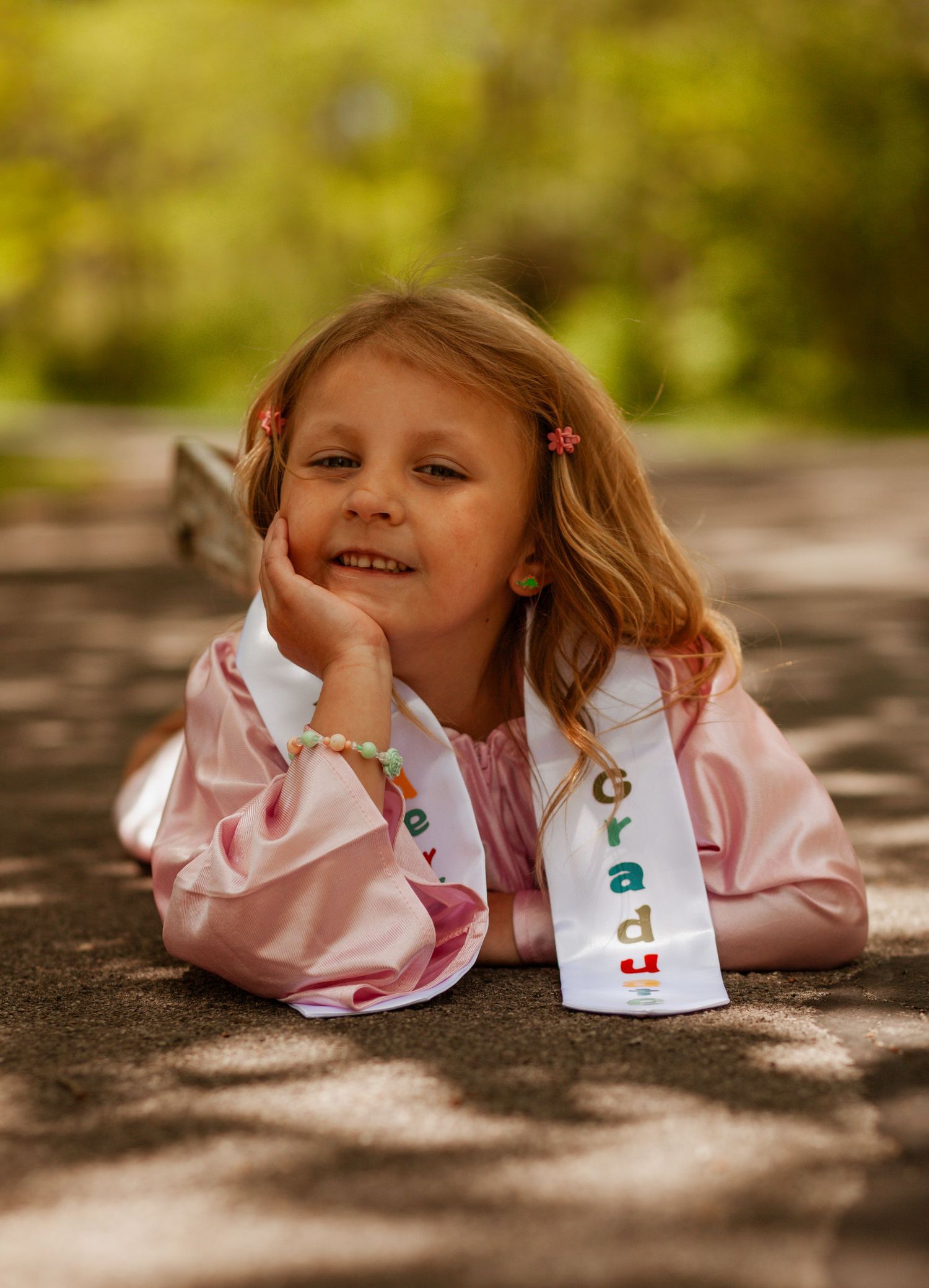 A playful sequence of a child in pink lying on a textured surface outdoors.