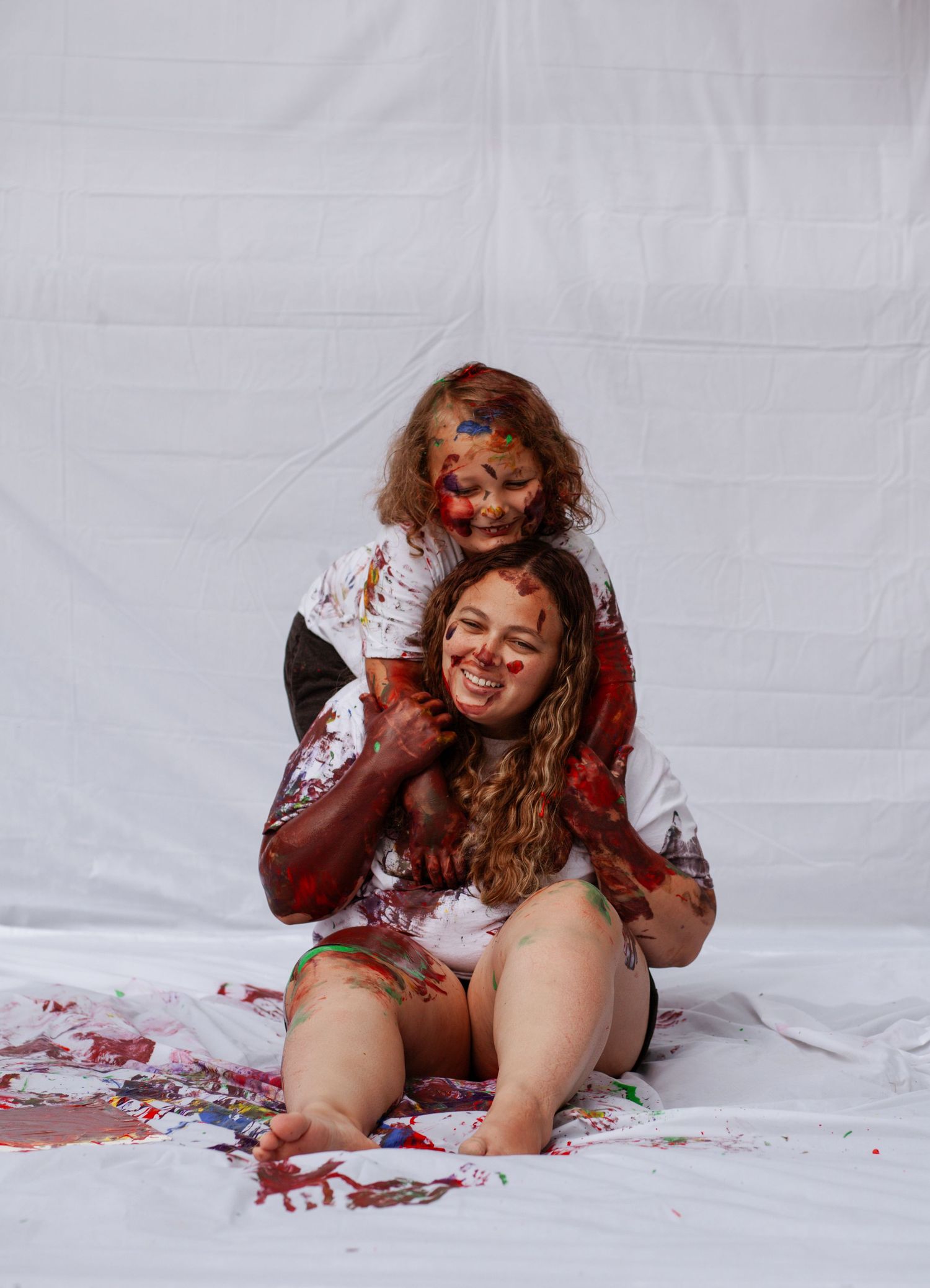 Joyful messy paint play session on white backdrop with splashes of red.