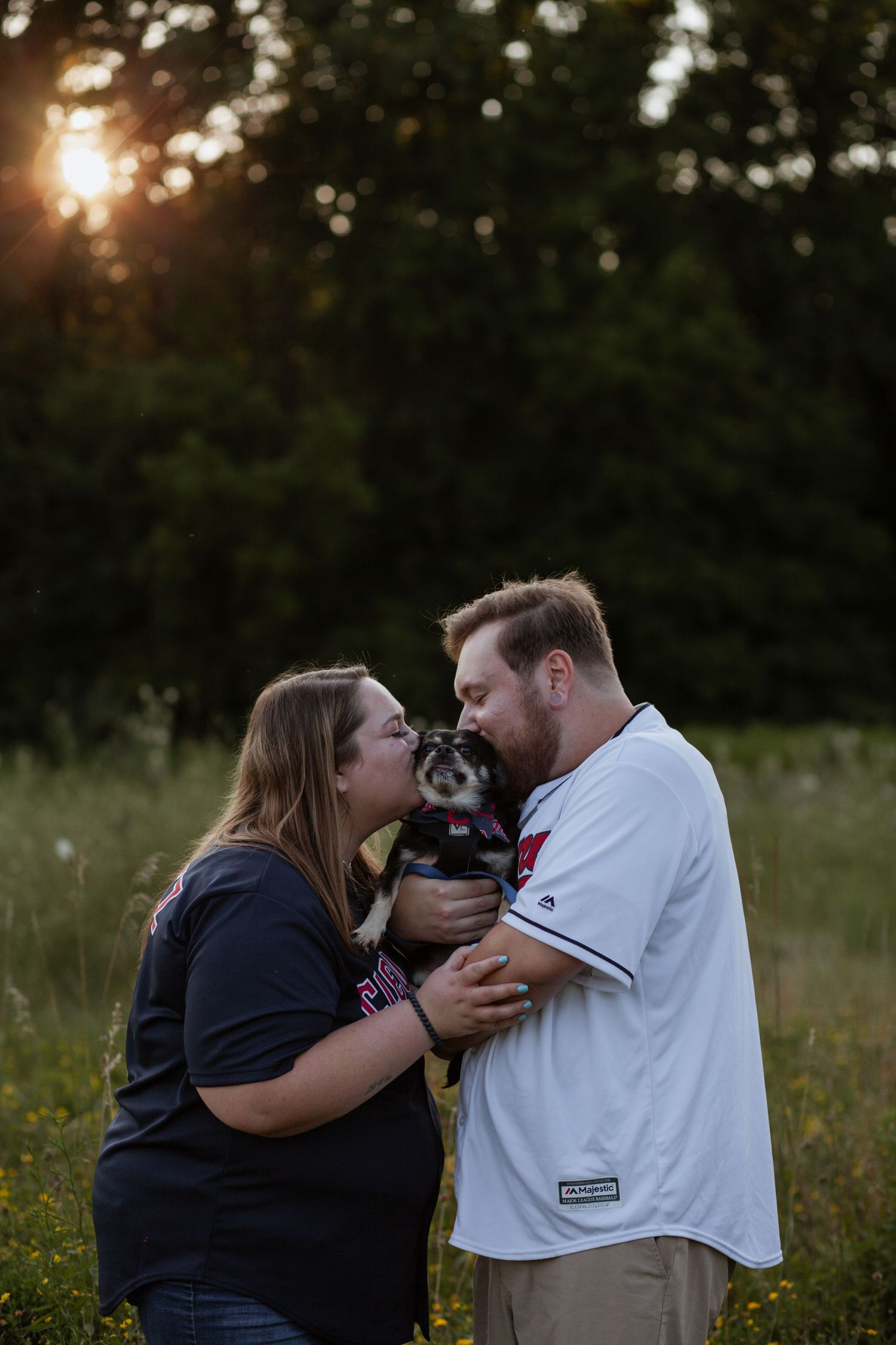 Couple sharing tender moments with their pet in a sunset field.