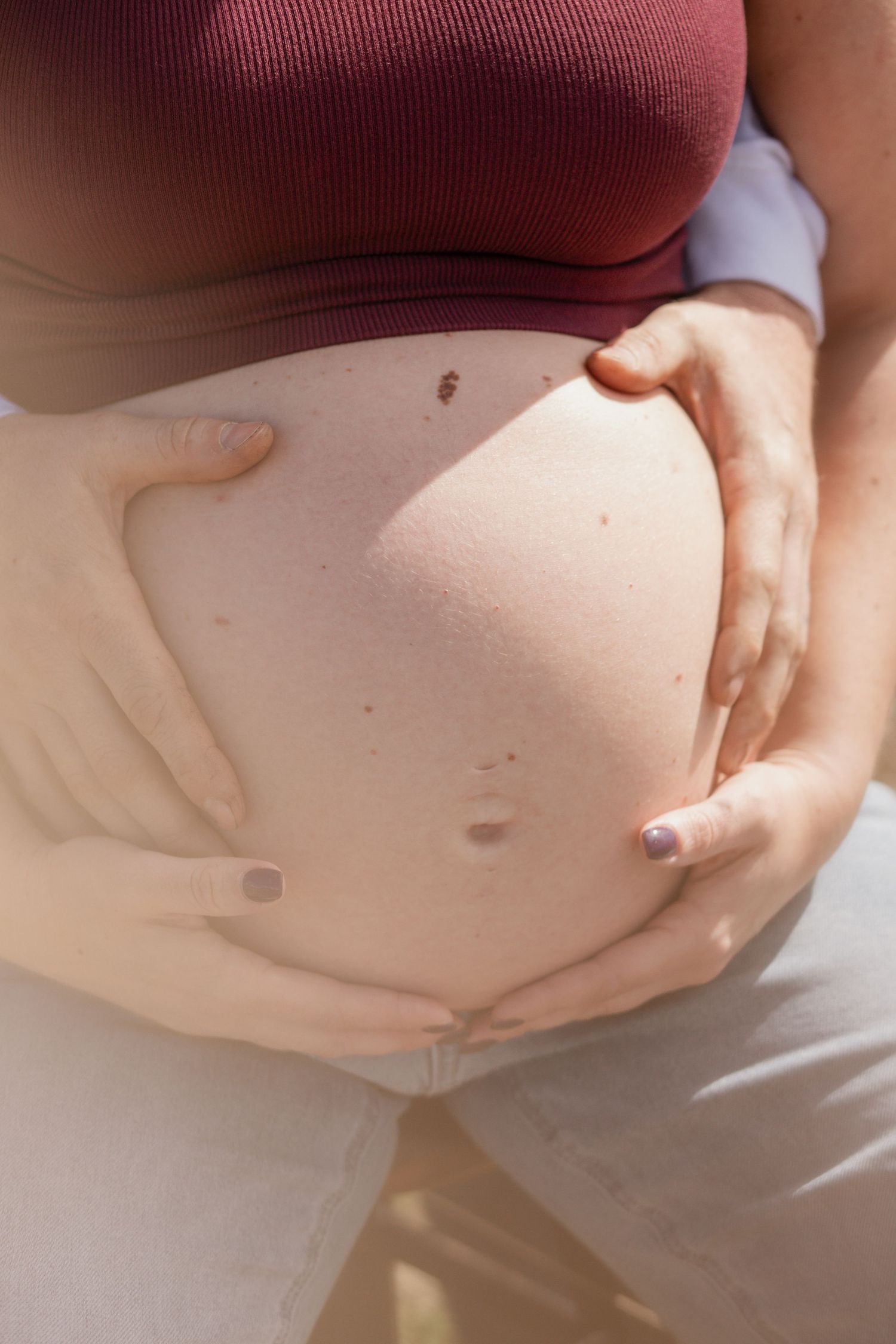 Series of close-up shots showing hands tenderly holding a pregnant belly in burgundy top.