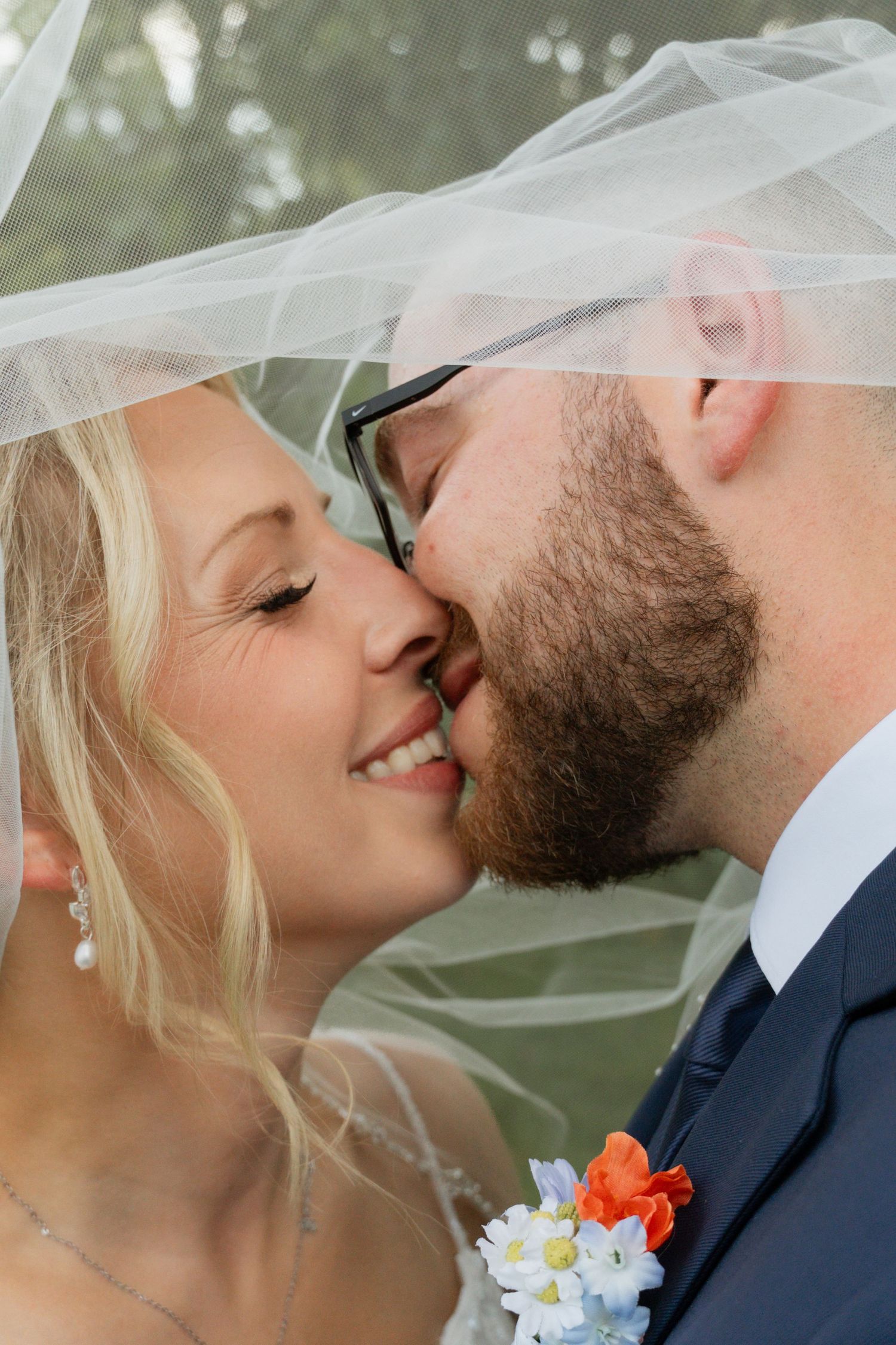 Romantic wedding couple sharing a tender kiss under a delicate veil with floral accents.