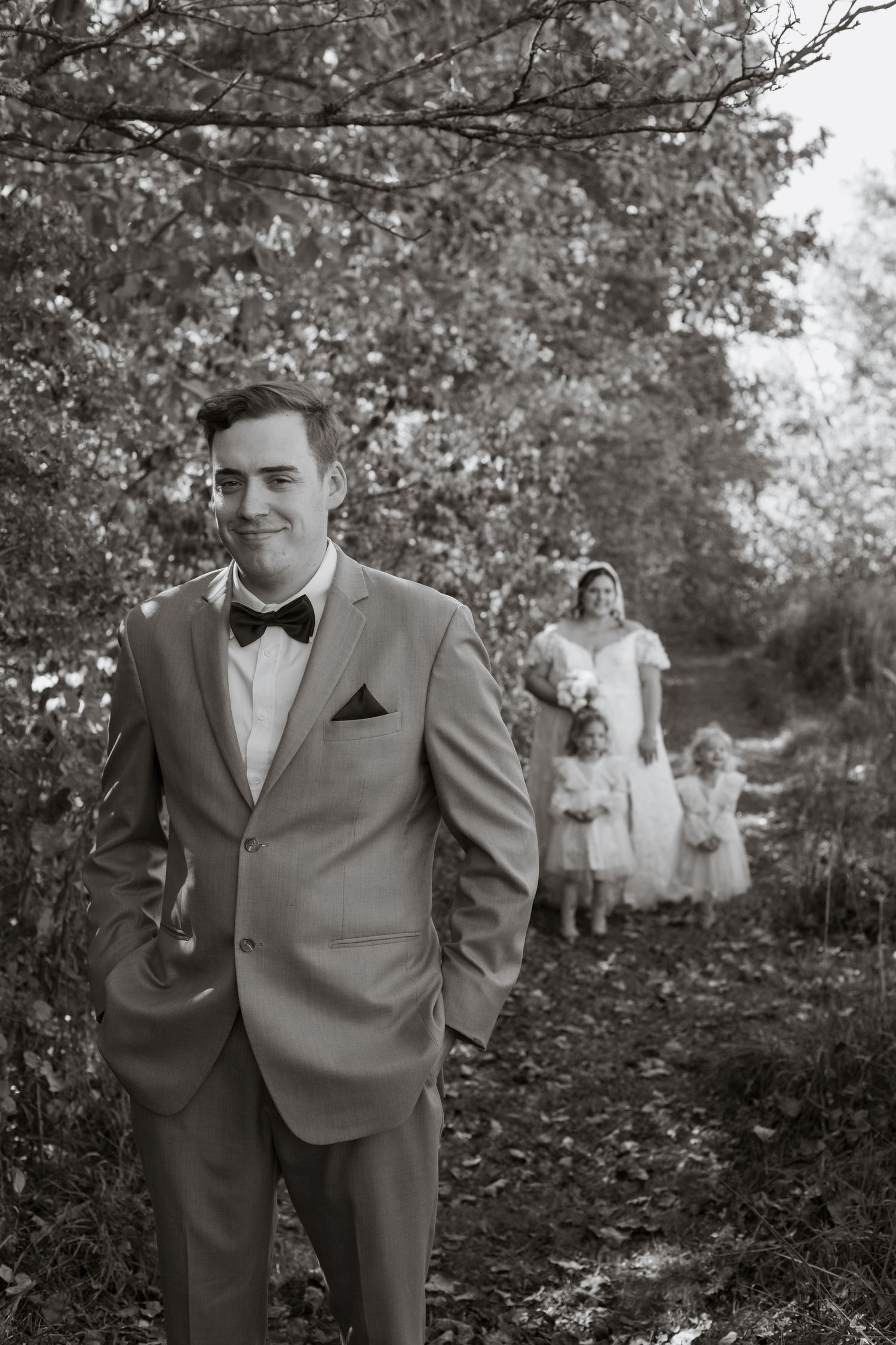 Black and white portrait in formal attire against a natural wooded backdrop.