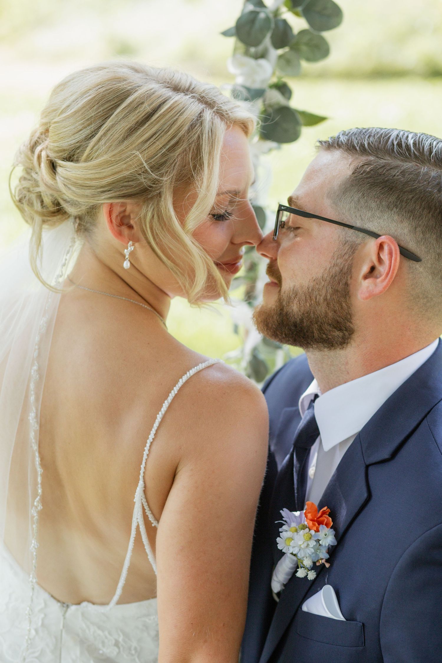 Intimate wedding portrait showing a tender moment between newlyweds with a floral boutonniere against a soft outdoor backdrop.