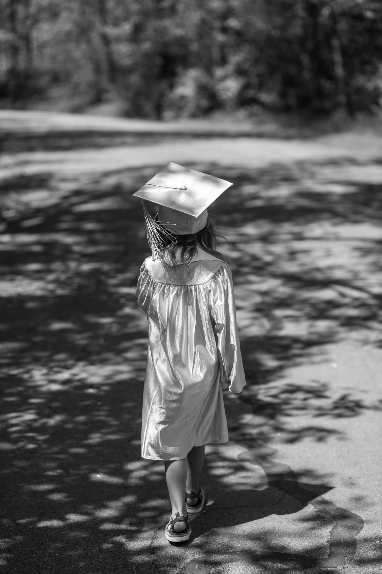 A black and white photo sequence of a small graduate walking away in a cap and gown.