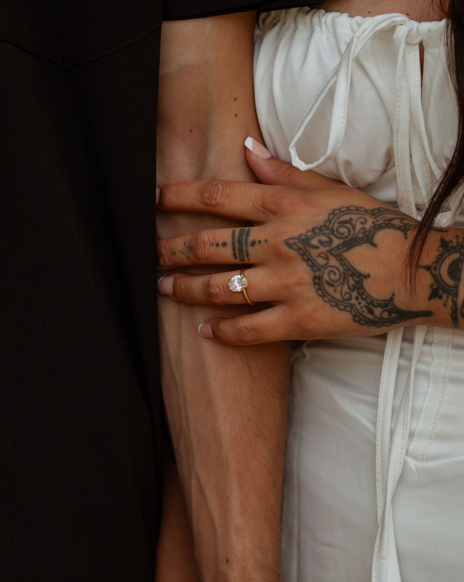 Close-up view of tattooed hands wearing a white dress and engagement ring.