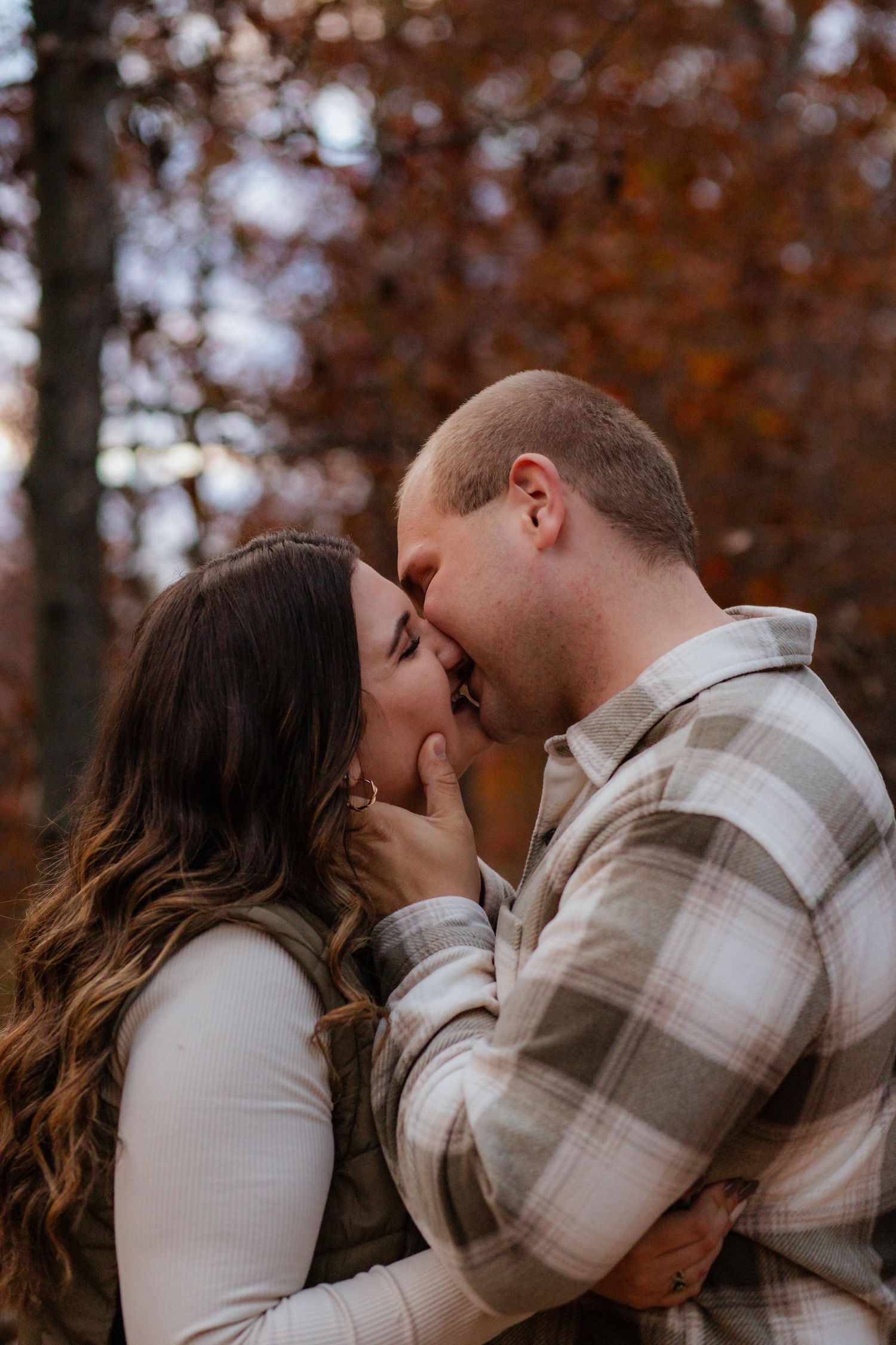A couple sharing a romantic kiss surrounded by fall foliage in warm autumn lighting.