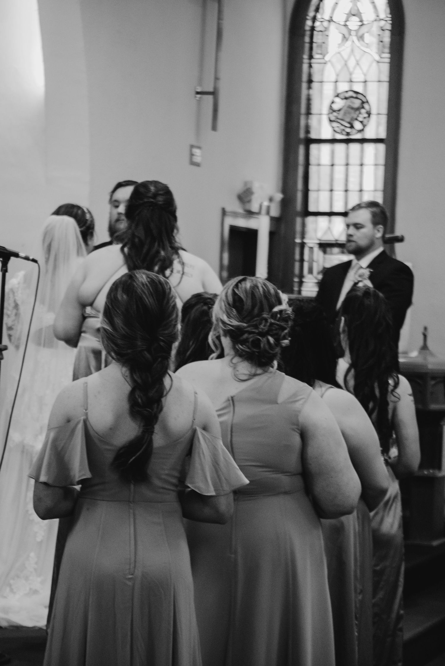 Bridesmaids in matching mauve dresses stand in church during ceremony.