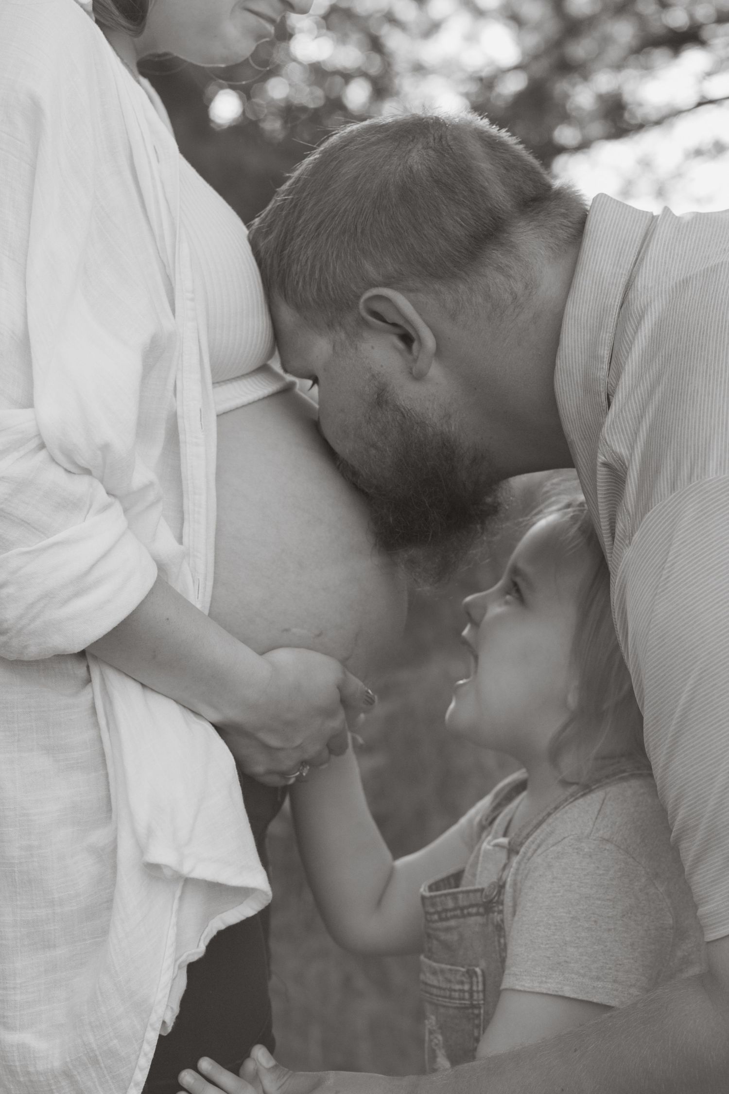 Tender maternity moment with family gathered around pregnant belly in soft lighting.