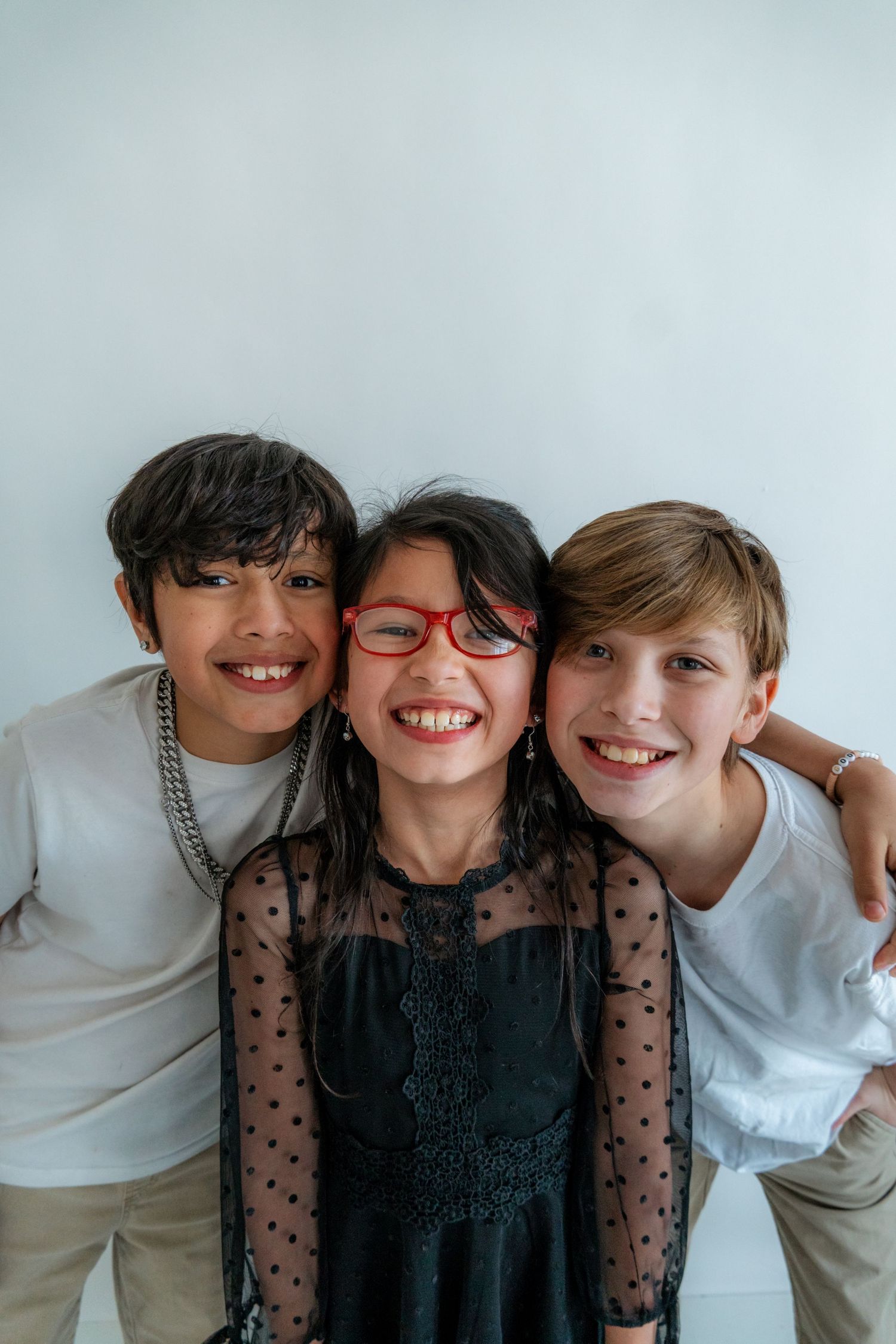 Three siblings posing playfully together against a white background.